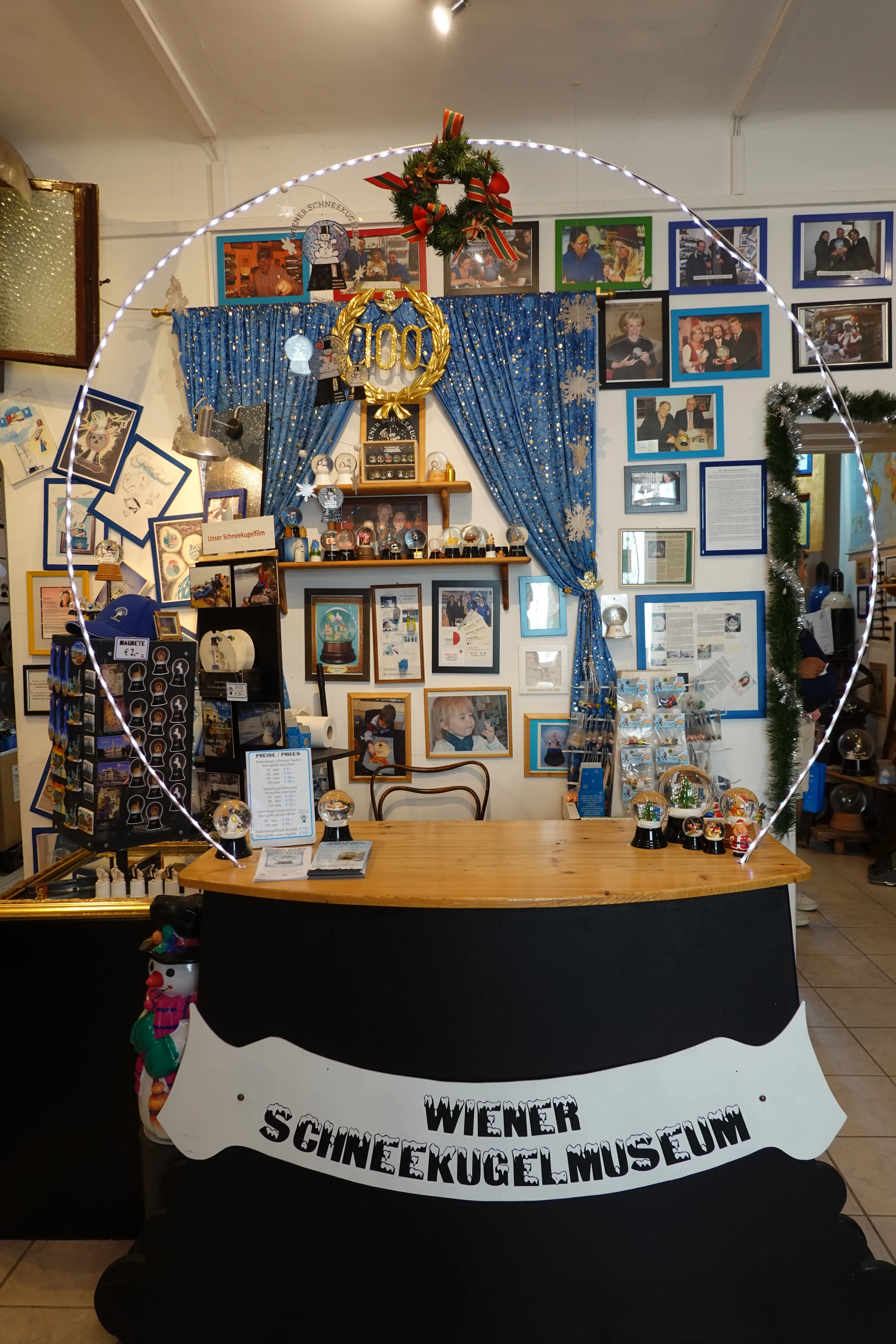 Interior of the Wiener Schneekugelmuseum with a reception desk, snow globes, and framed photos on the walls