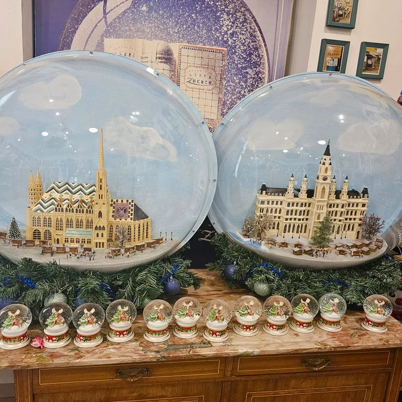 Two large snow globes displaying miniature scenes of Vienna buildings, surrounded by smaller snow globes on a wooden cabinet