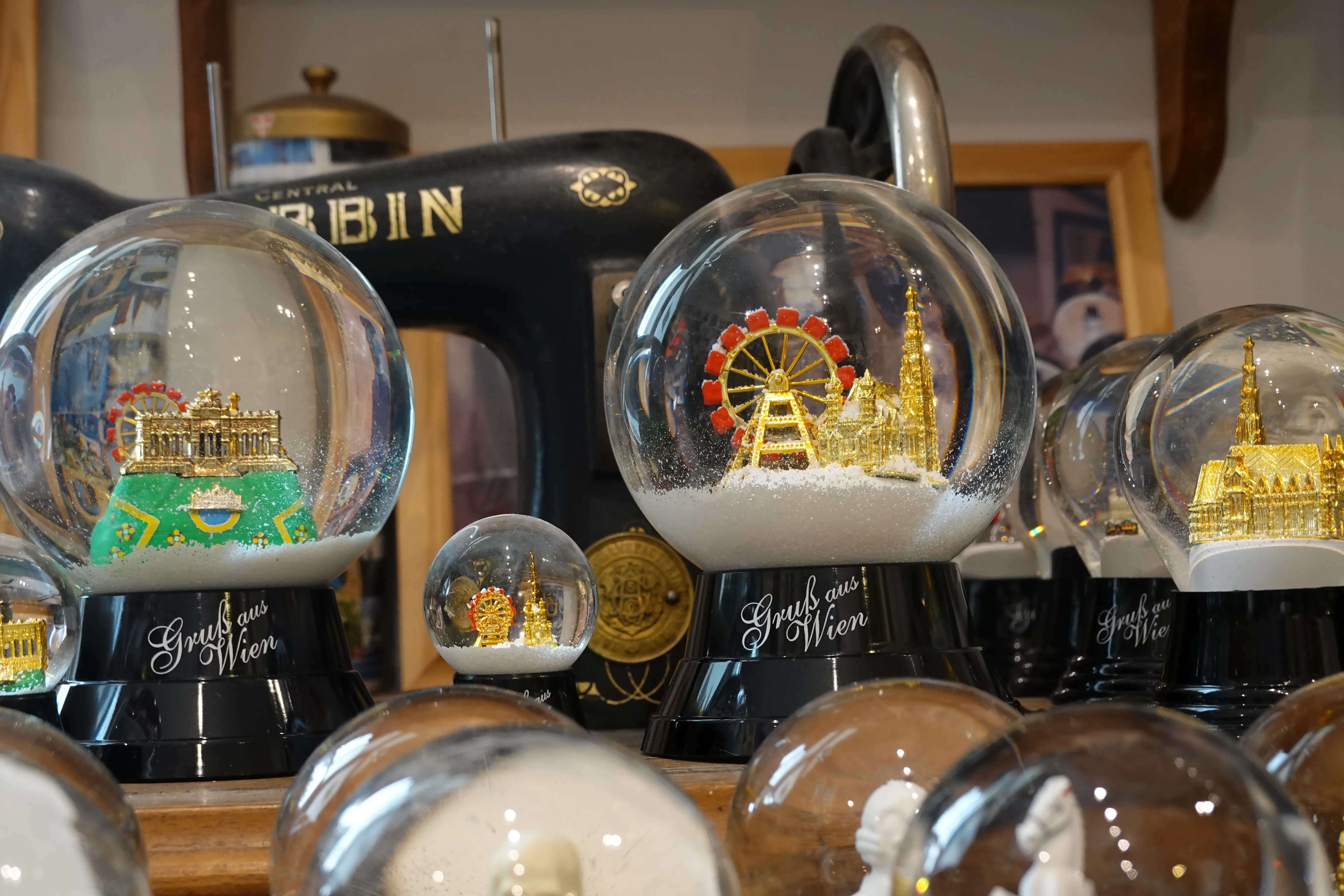 Viennese snow globes with miniature city scenes, including a Ferris wheel and cathedral, displayed on black bases with text.