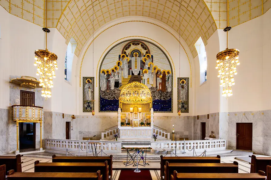 Wnętrze kościoła Otto Wagnera w Steinhof z dużym mozaiką nad ołtarzem, żyrandolami i drewnianymi ławkami.