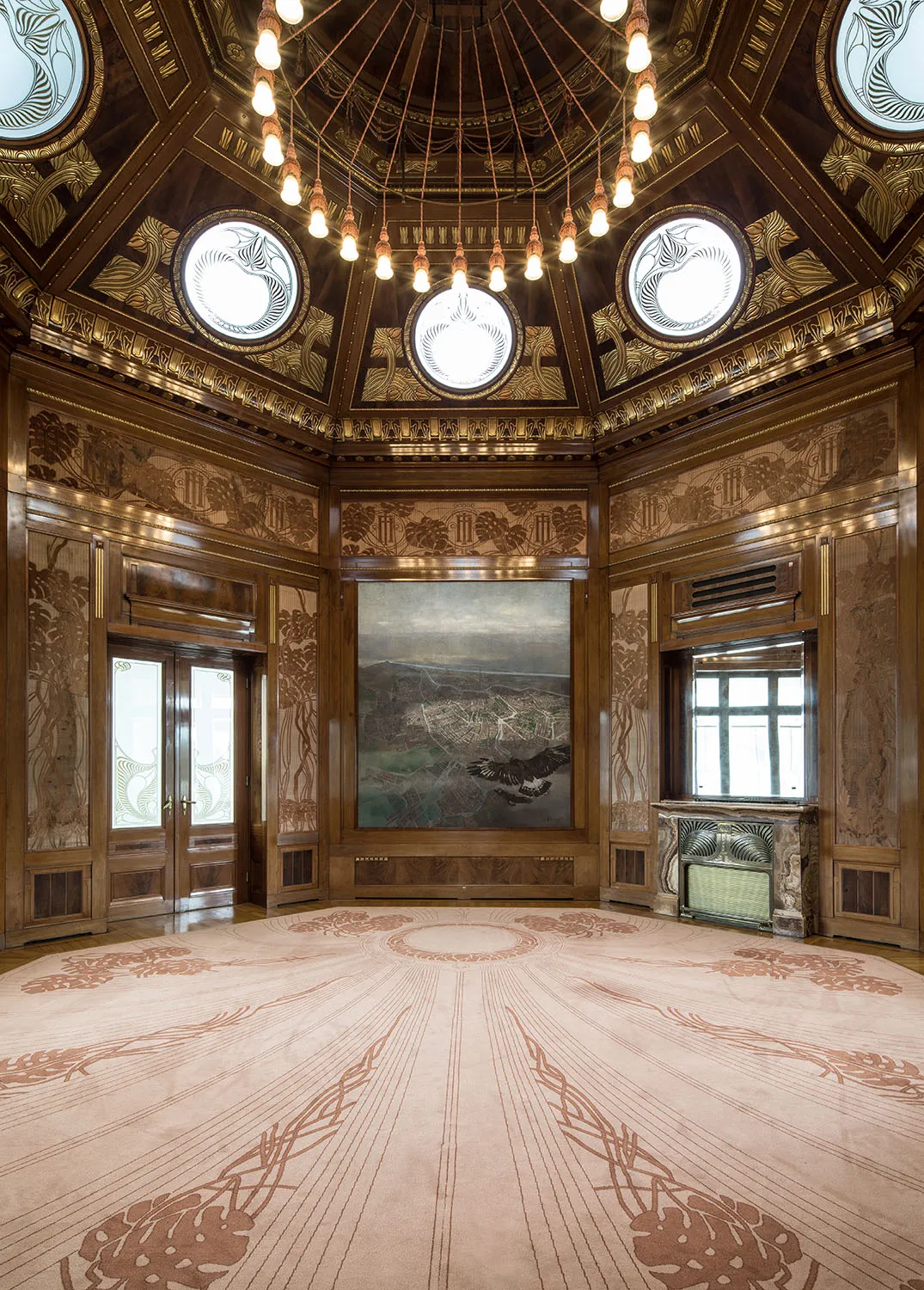 Sierlijk interieur van een grote zaal met een koepelvormig plafond, cirkelvormige dakramen, gouden details, houten lambrisering en een groot schilderij aan de muur