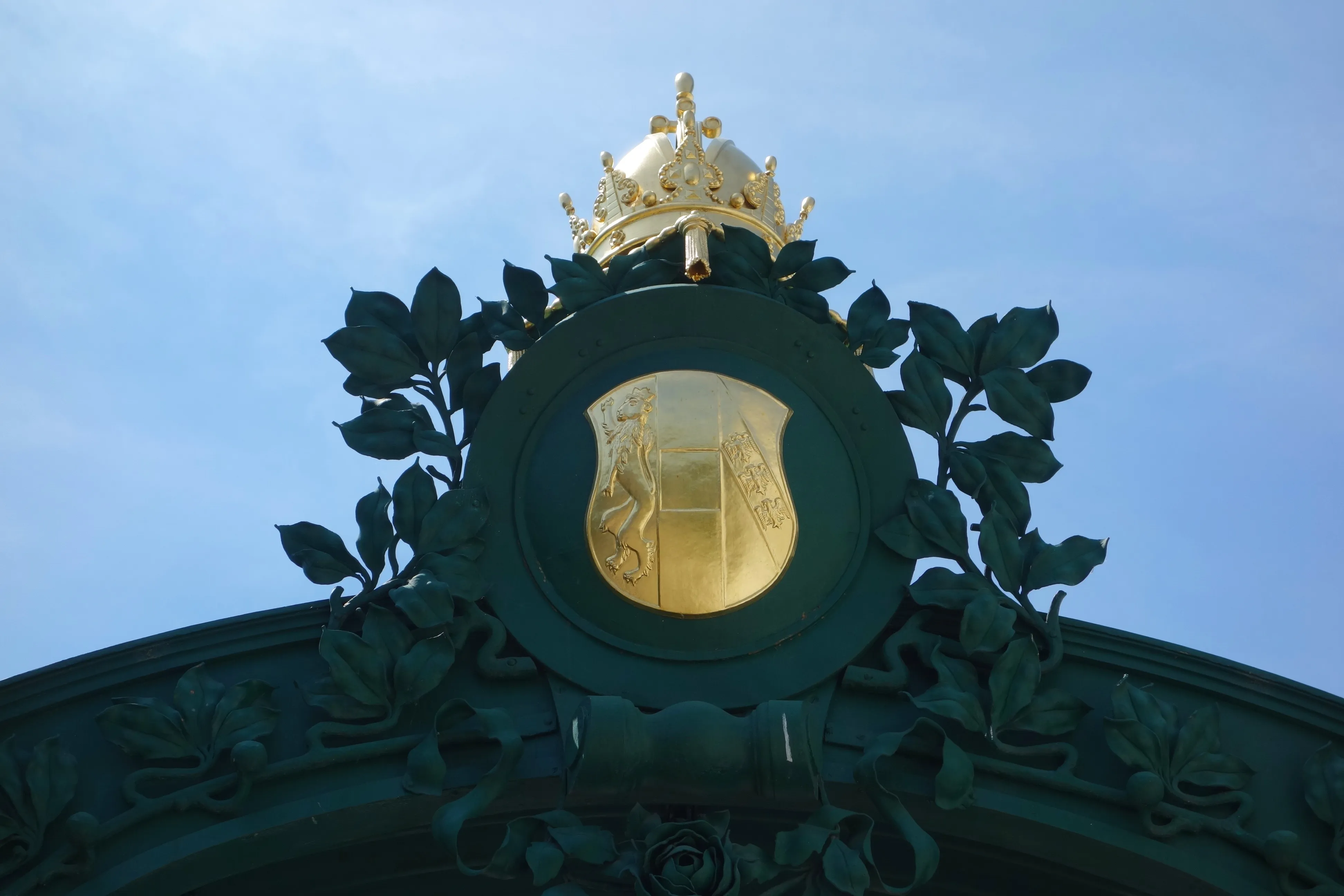 Gouden kroon en keizerlijk embleem op een groen architectonisch detail tegen een blauwe hemel