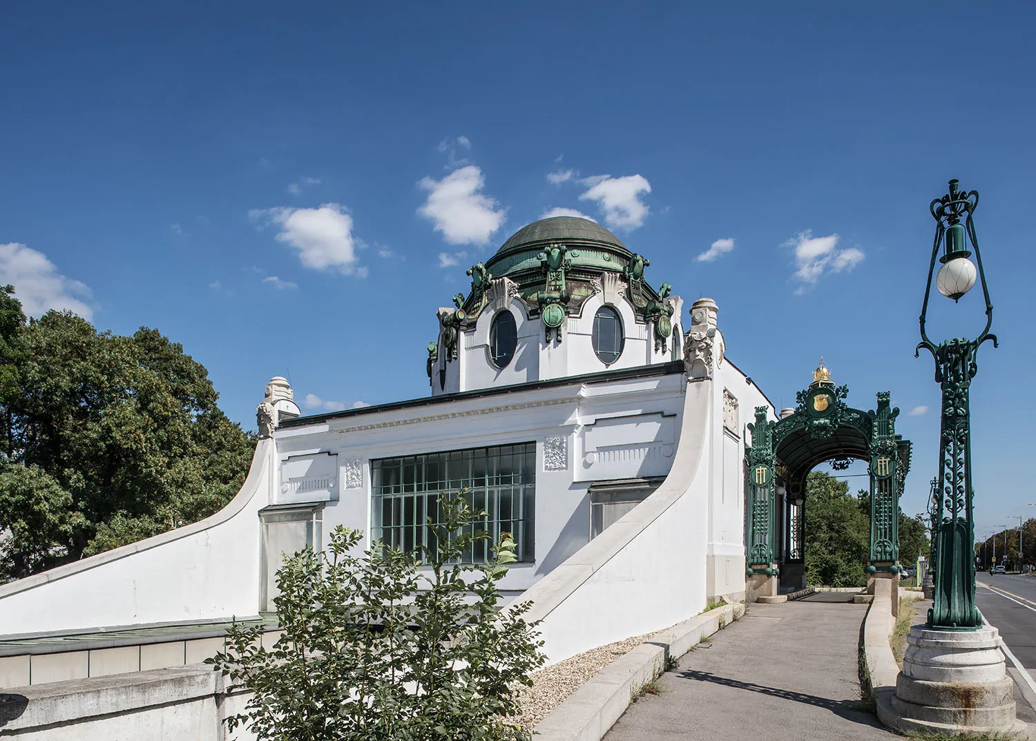 Wit Art Nouveau paviljoen met groene koepel en decoratieve elementen onder een blauwe hemel