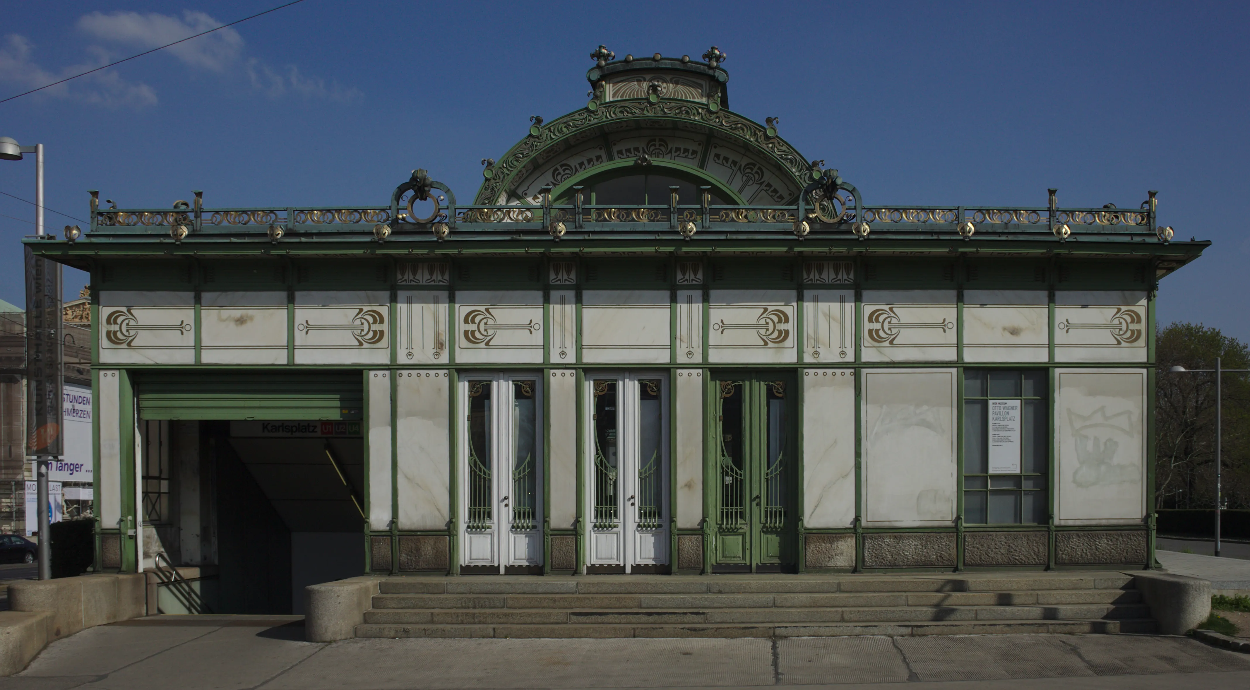 Art Nouveau pavilion with green and white facade, arched entrance, and decorative roofline under a blue sky