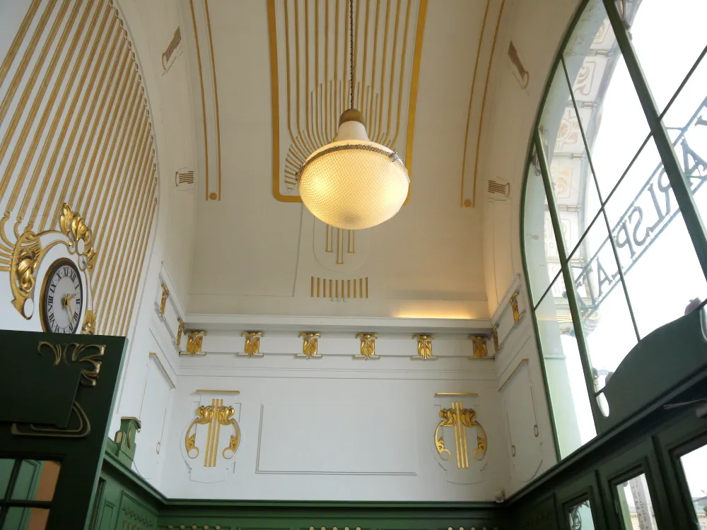 Interior Art Nouveau con detalles dorados, una lámpara colgante y ventanas arqueadas