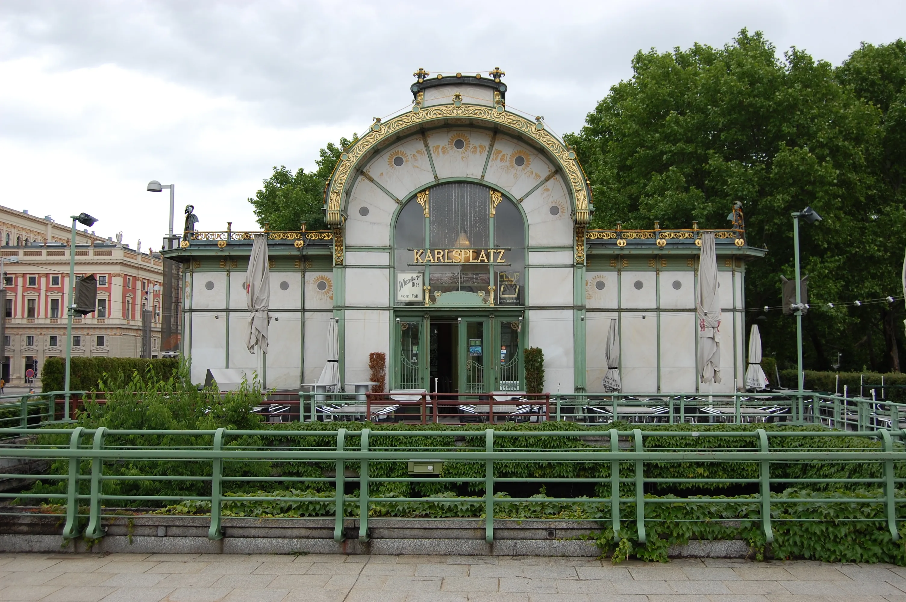 Art Nouveau pavilion with gold trim and arched entrance labeled Karlsplatz, surrounded by green railings and trees