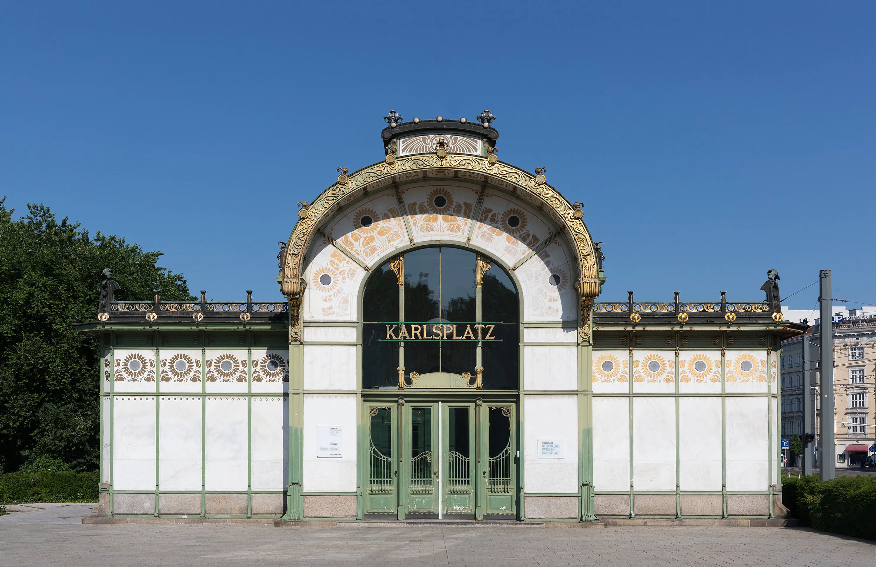 Pabellón Art Nouveau con detalles ornamentales dorados y una gran entrada arqueada etiquetada como KARLSPLATZ bajo un cielo azul claro