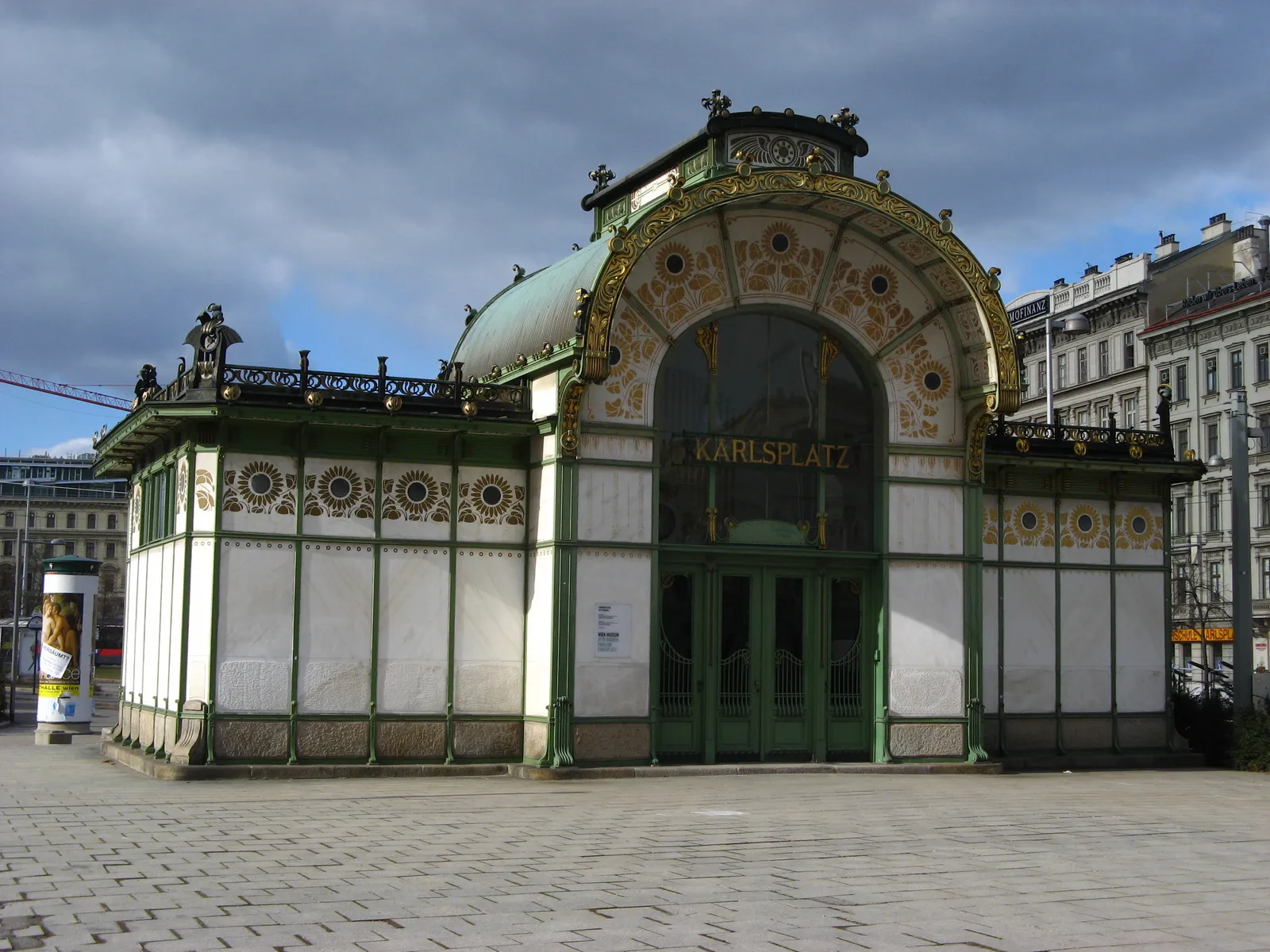 Pabellón Art Nouveau con fachada verde y blanca, entrada arqueada y ornamentación dorada sobre un cielo nublado