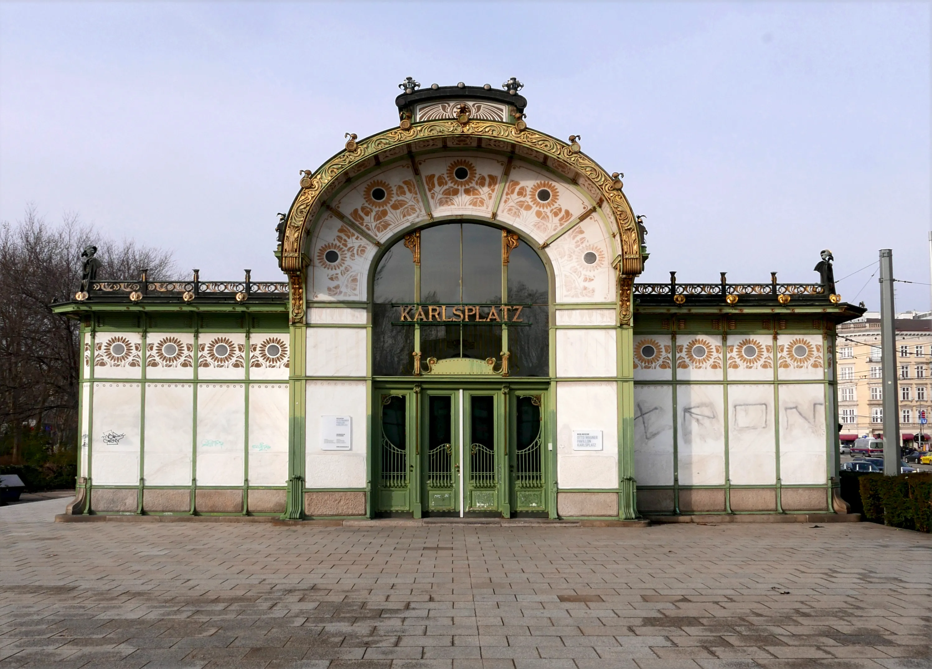 Pabellón Art Nouveau con fachada de azulejos verdes y blancos, entrada arqueada y letrero 'KARLSPLATZ' sobre las puertas
