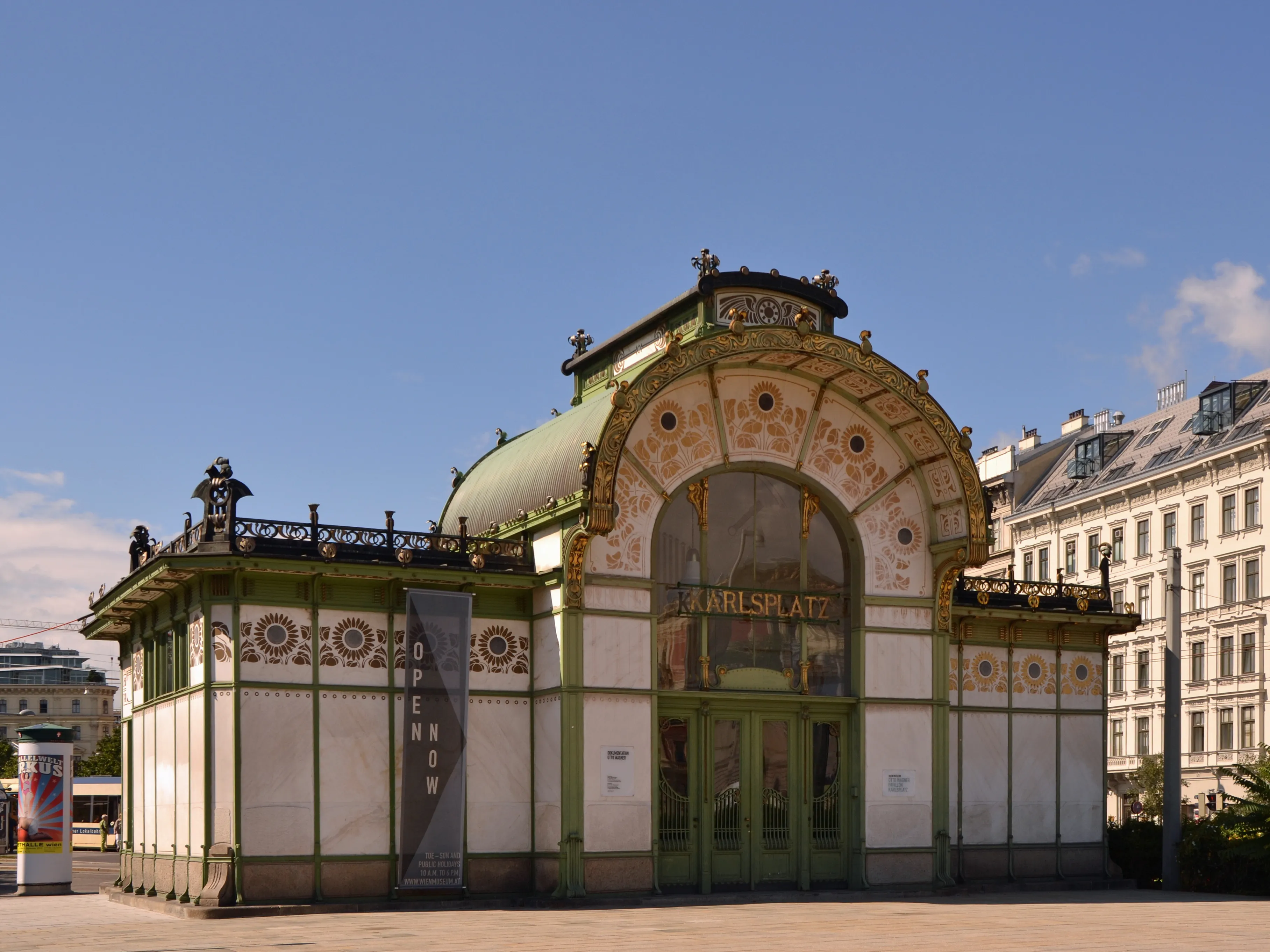 Pabellón de Art Nouveau con fachada verde y blanca, entrada de cristal arqueada y patrones decorativos bajo un cielo azul