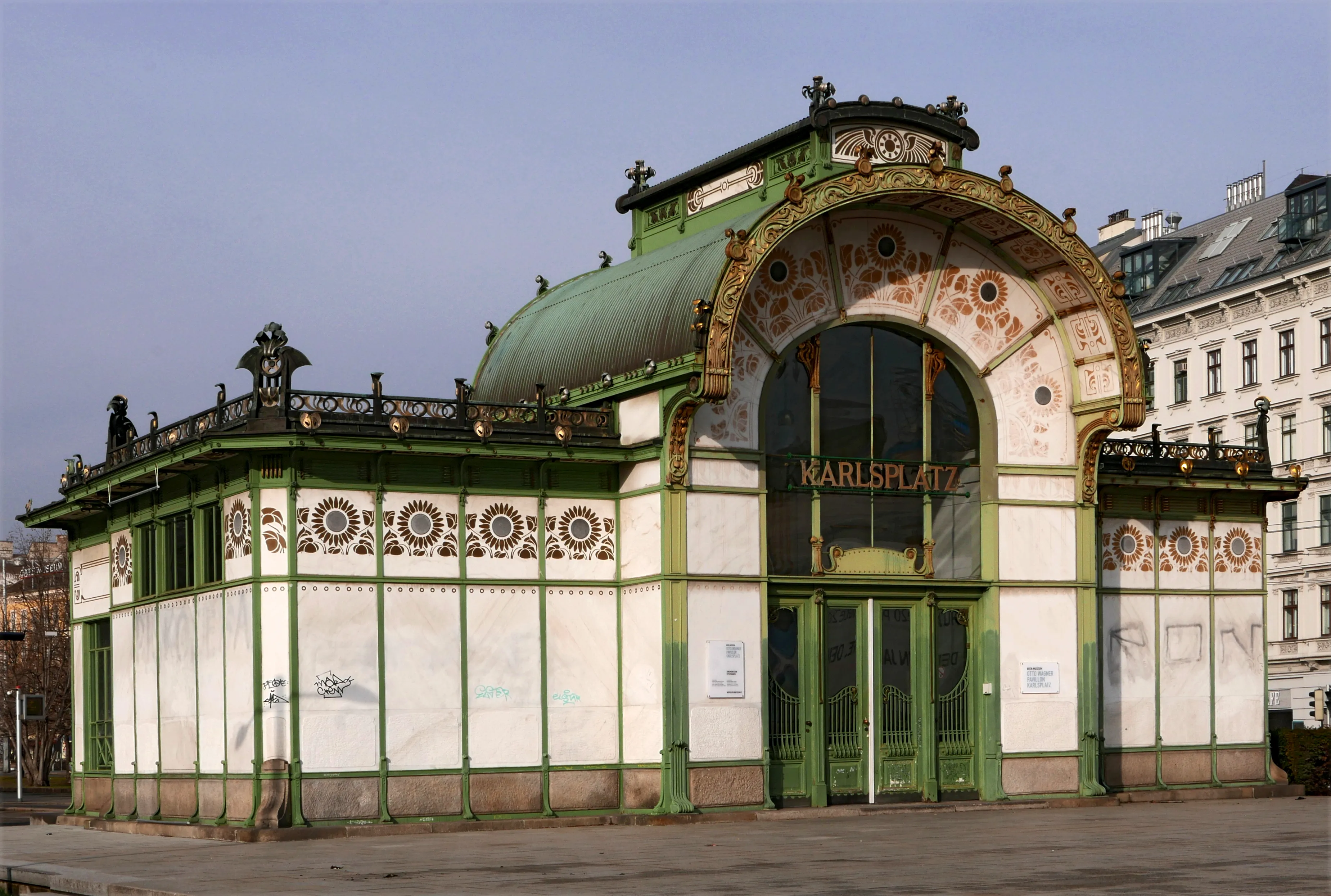 Pabellón Art Nouveau con fachada verde y blanca, entrada arqueada y elaborados patrones de azulejos, etiquetado Karlsplatz
