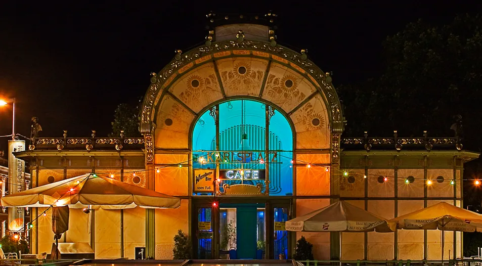 Pabellón Art Nouveau por la noche con entrada arqueada iluminada y zona de asientos al aire libre