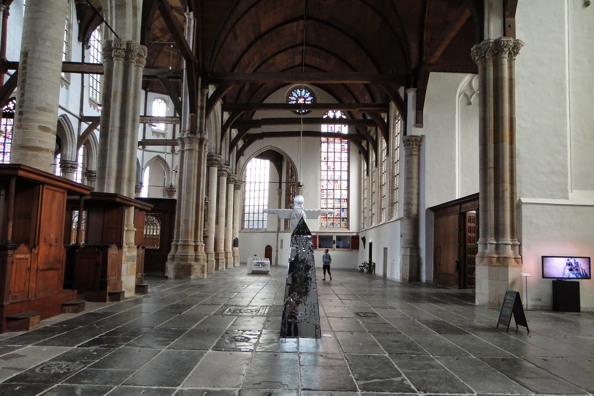 Interior of Oude Kerk with high wooden beams, stone columns, and a modern art sculpture on a tiled floor