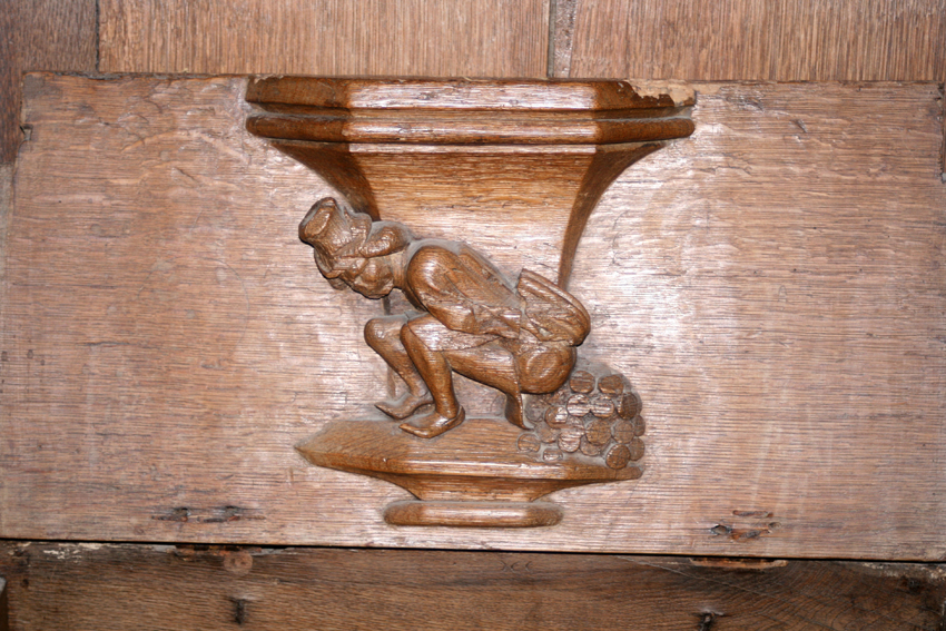 carved wooden misericord with a figure in a crouched position