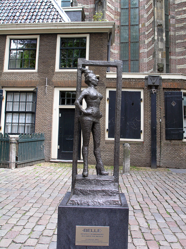 Estatua de bronce 'Belle' de una mujer desnuda en una estructura de marco sobre adoquines frente a la fachada de ladrillos de la Oude Kerk en Ámsterdam