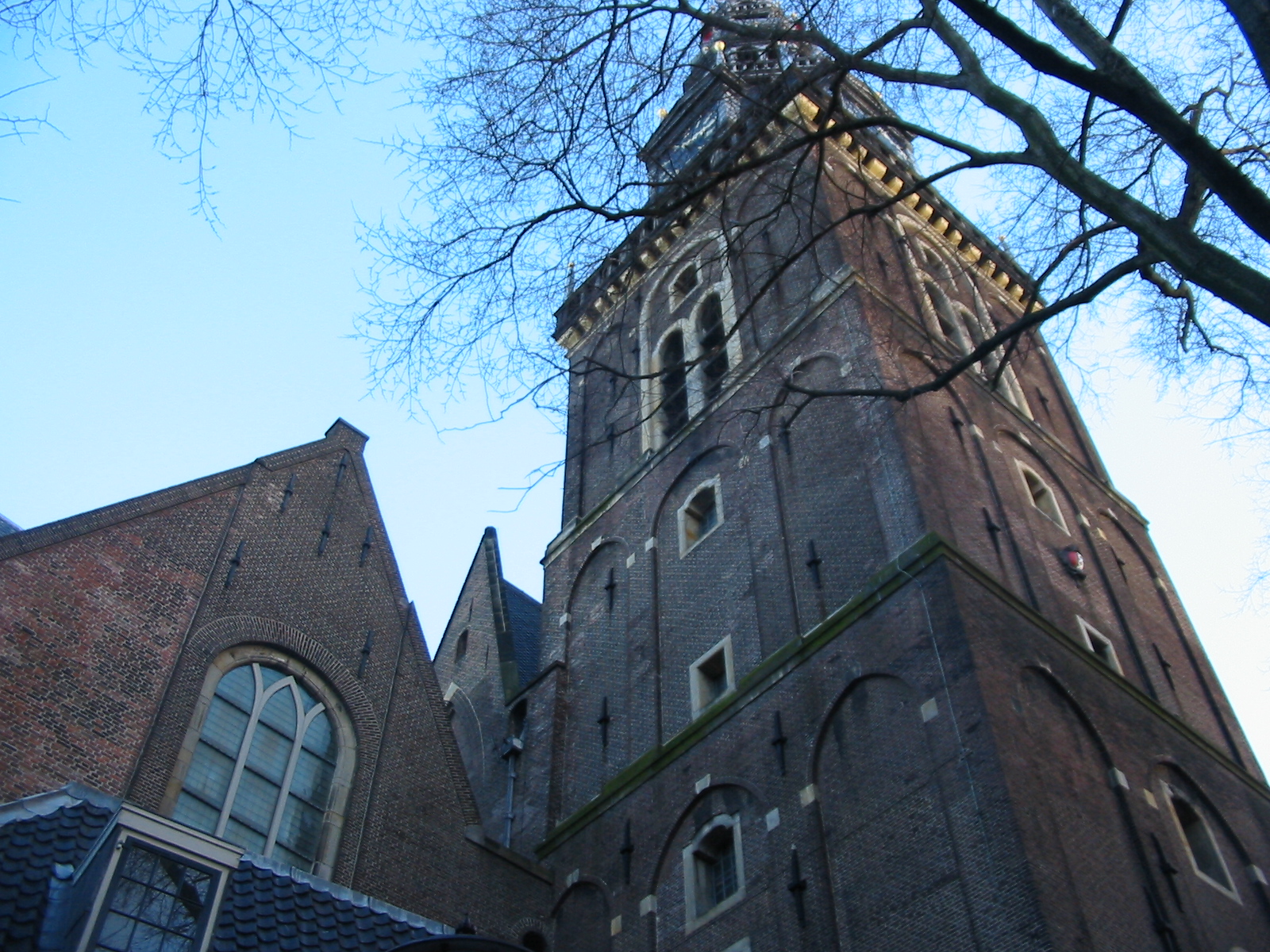 Tall brick church tower with arched windows and a clock, surrounded by bare tree branches under a clear blue sky.