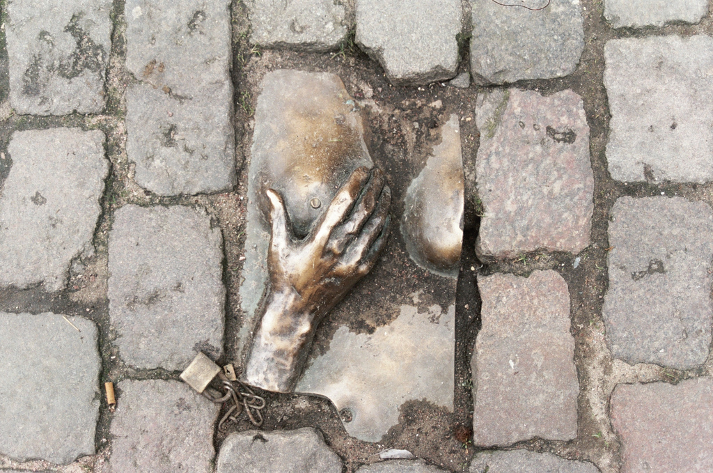 Bronze relief of a hand reaching up from a cobblestone street