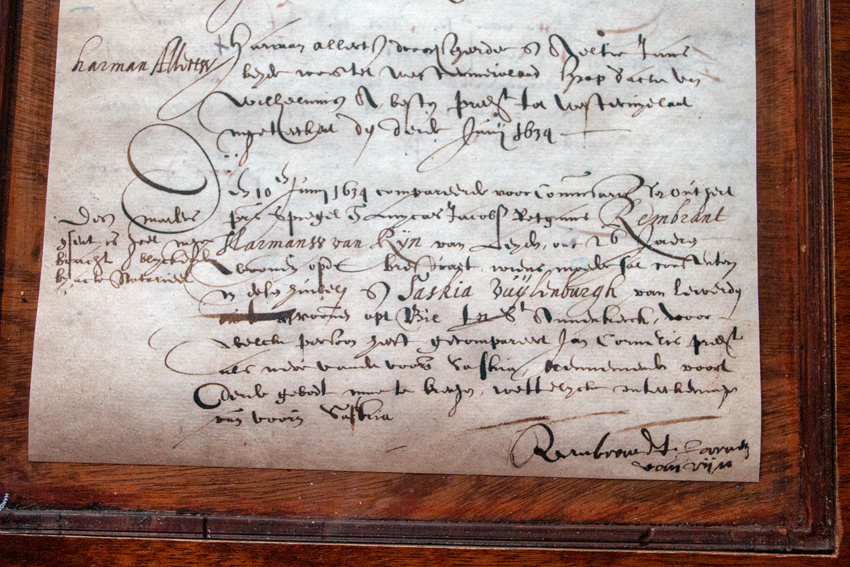 Manuscrito histórico enmarcado con escritura cursiva ornamentada sobre pergamino envejecido, expuesto en un marco de madera