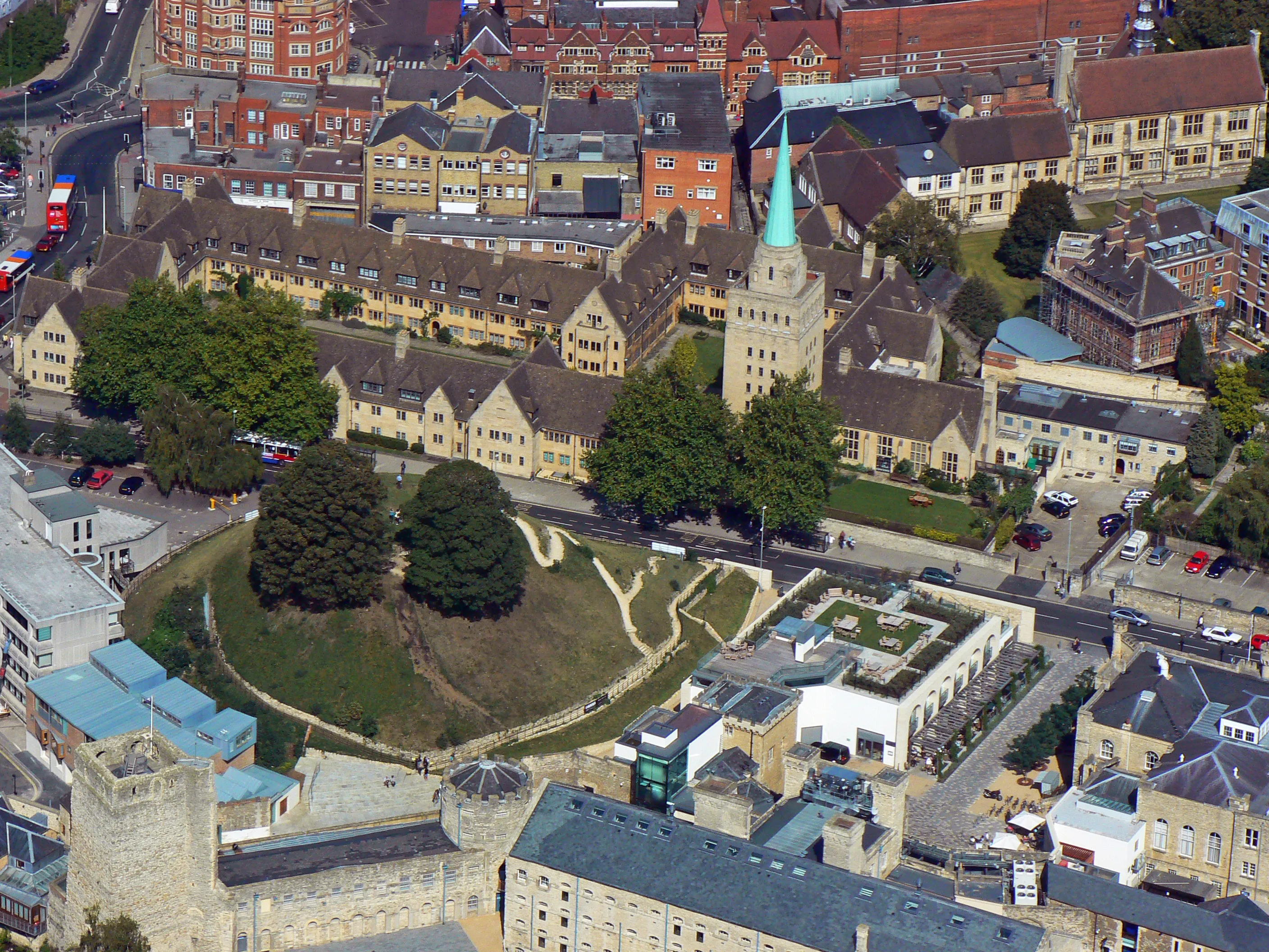 Vista aérea de la colina del Oxford Castle y los edificios históricos circundantes, incluyendo una iglesia con una aguja verde.