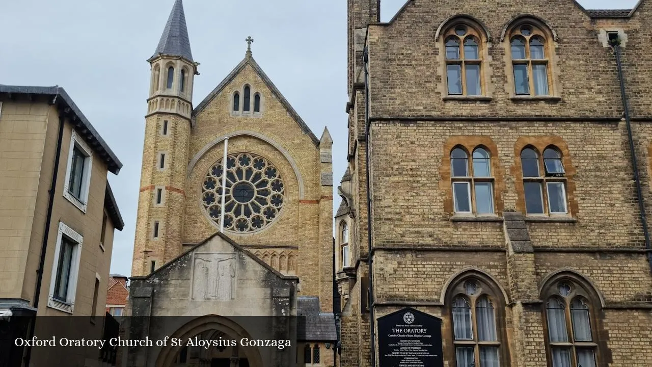 Vista exterior de la Oxford Oratory Church of St Aloysius Gonzaga que muestra una fachada de piedra con un gran rosetón, una torre con aguja puntiaguda y un edificio contiguo con ventanas de arco gótico y una placa azul de patrimonio histórico.