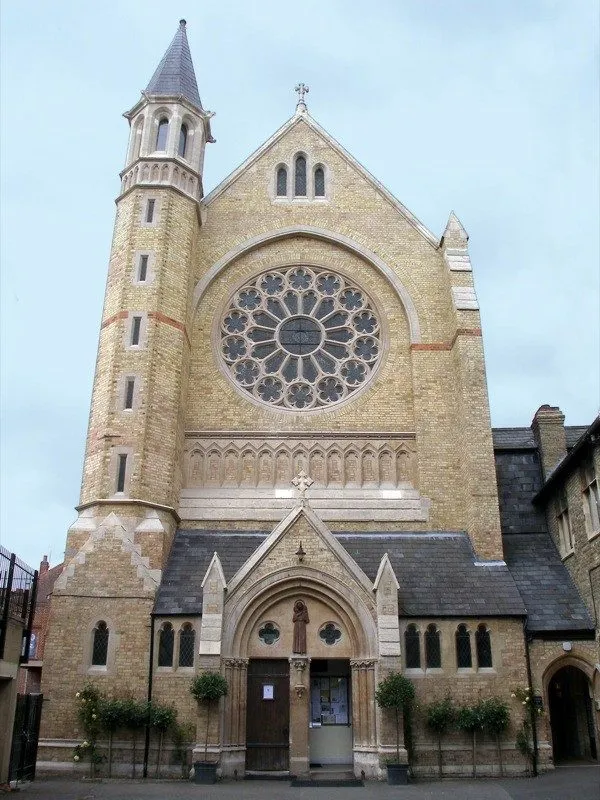 Fachada de iglesia neogótica con un gran rosetón, campanario de piedra y puerta de entrada en arco.