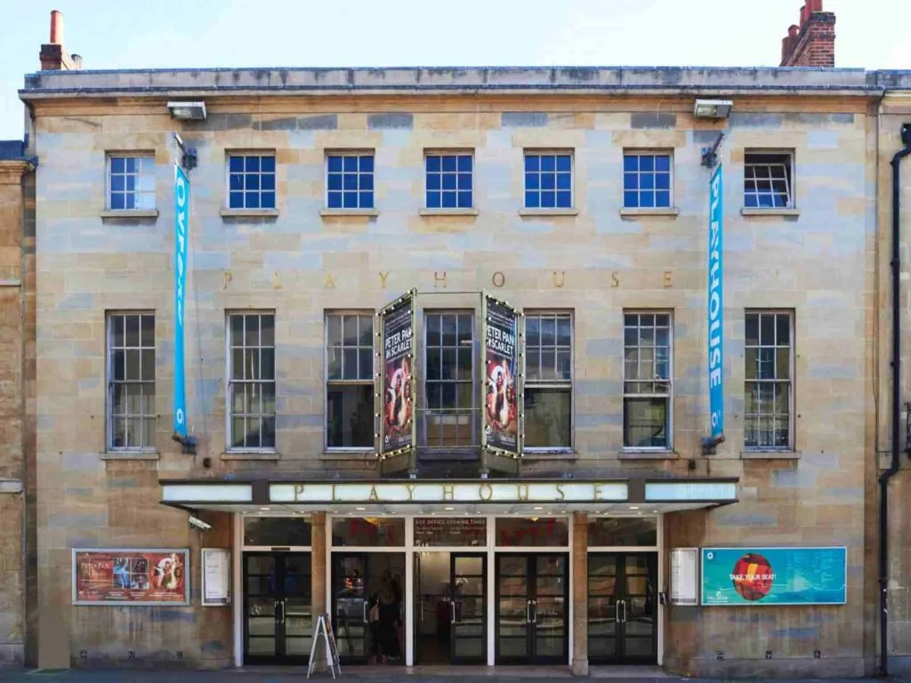 Fachada de piedra del teatro Oxford Playhouse con entrada con marquesina, pancartas verticales azules y carteles de espectáculos