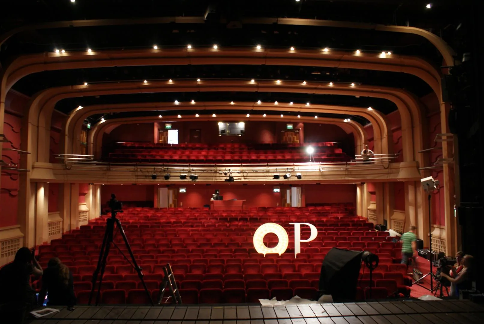 Auditorio del Oxford Playhouse con asientos rojos en niveles, varios niveles de balcones, iluminación cálida y el logotipo de OP visible en el escenario