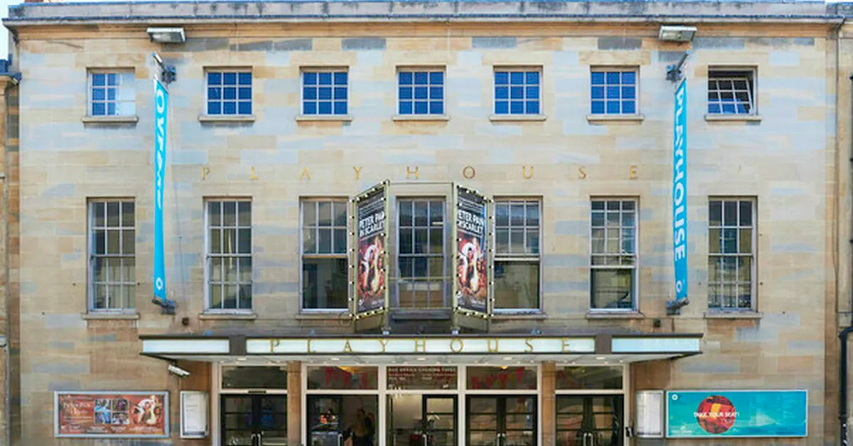 Fachada de piedra del teatro Oxford Playhouse con múltiples ventanas, pancartas azules colgantes y carteles exhibidos sobre la marquesina de la entrada
