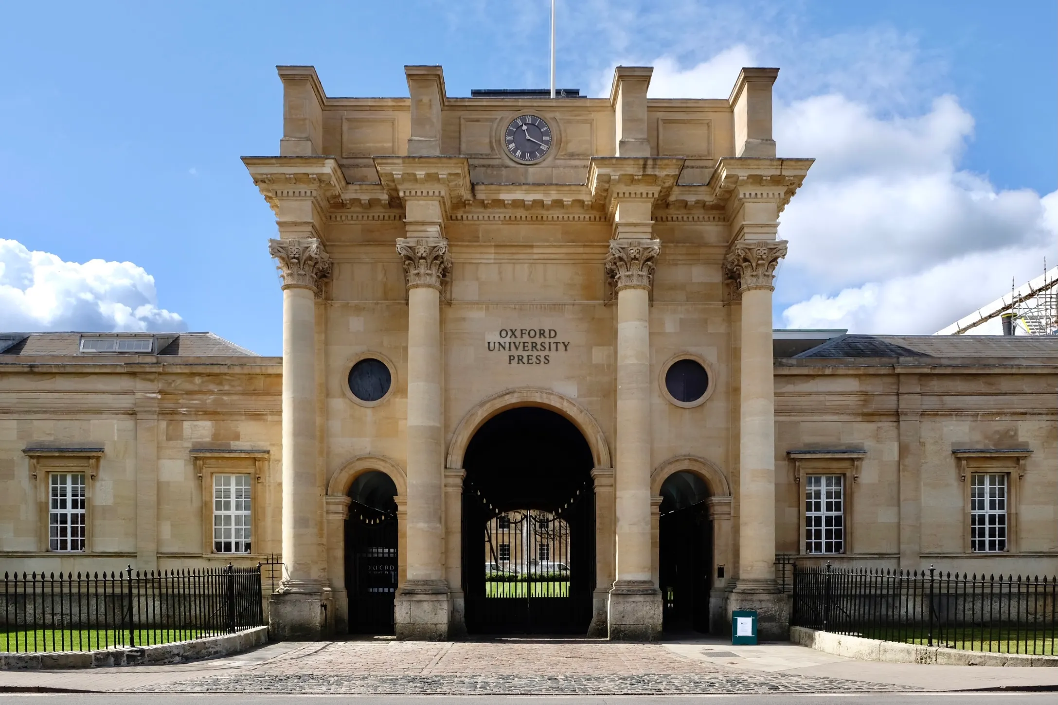 Klasyczna kamienna brama wejściowa budynku Oxford University Press przy Walton Street, z kolumnami, zegarem, łukowatą bramą i napisem 'Oxford University Press' na fasadzie pod błękitnym niebem