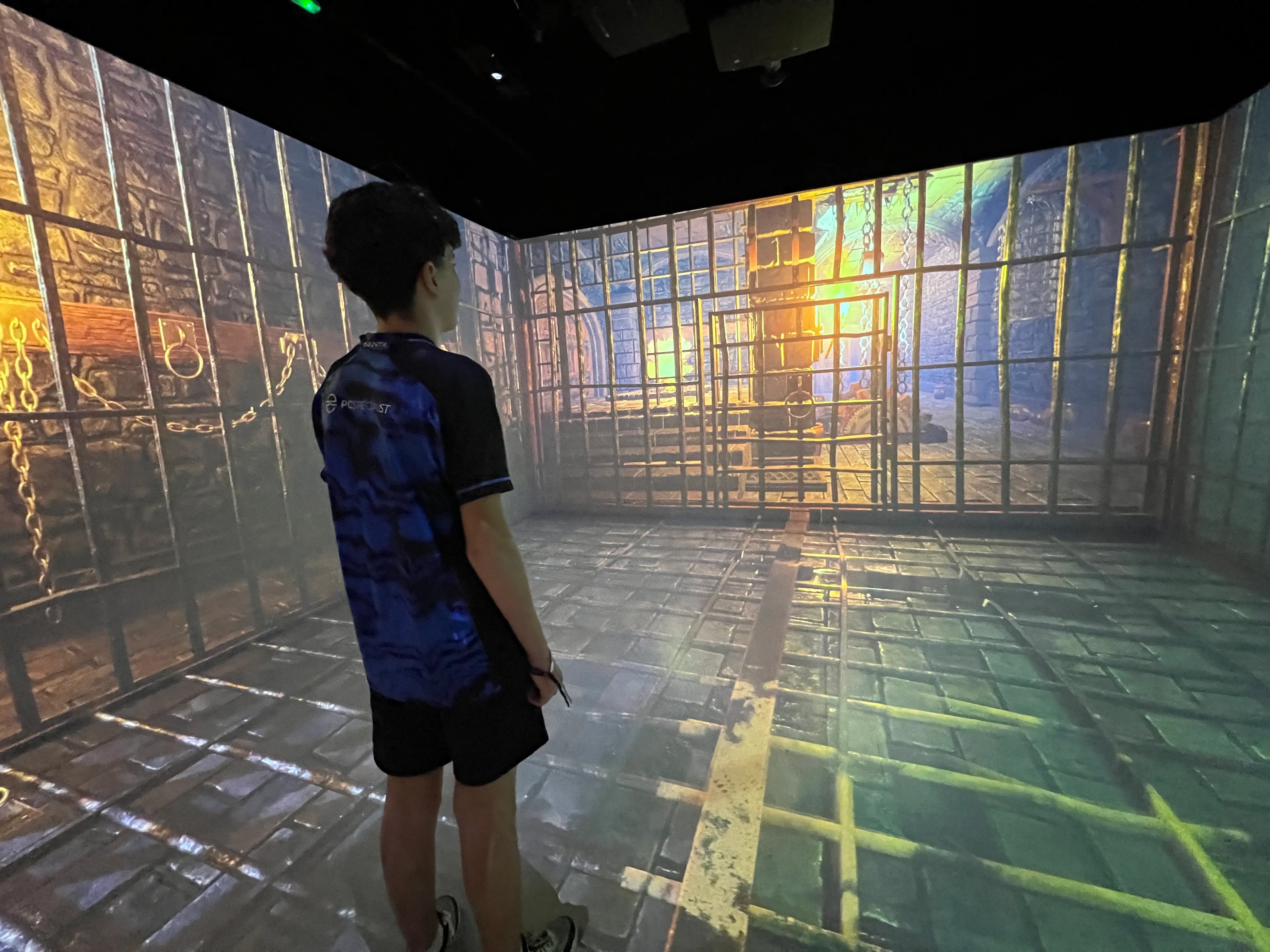 Un niño se encuentra dentro de una sala inmersiva oscura con imágenes de videojuegos proyectadas en las paredes, el suelo y el techo en el OXO Museo del Videojuego Málaga.