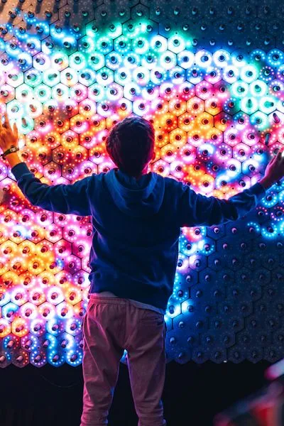 Person with arms outstretched facing a colorful, illuminated hexagonal light installation
