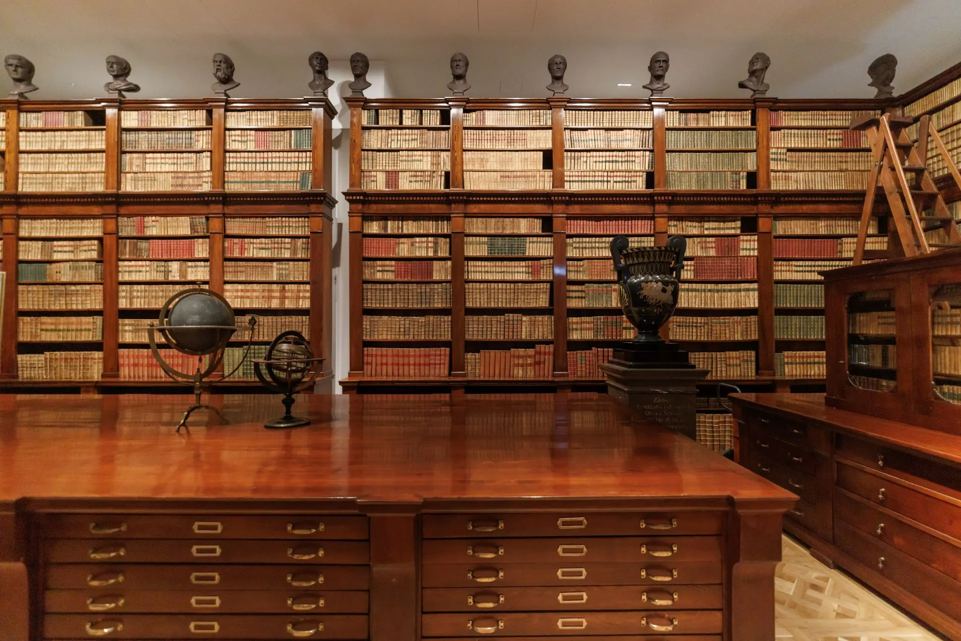 houten bibliotheek met boekenplanken, een bureau en bustes bovenop de planken