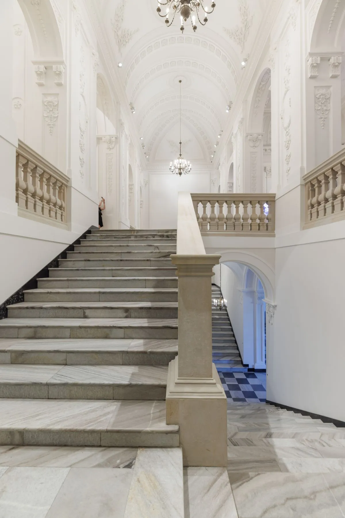 Marmeren trap in een grote hal met sierlijke witte muren en kroonluchters