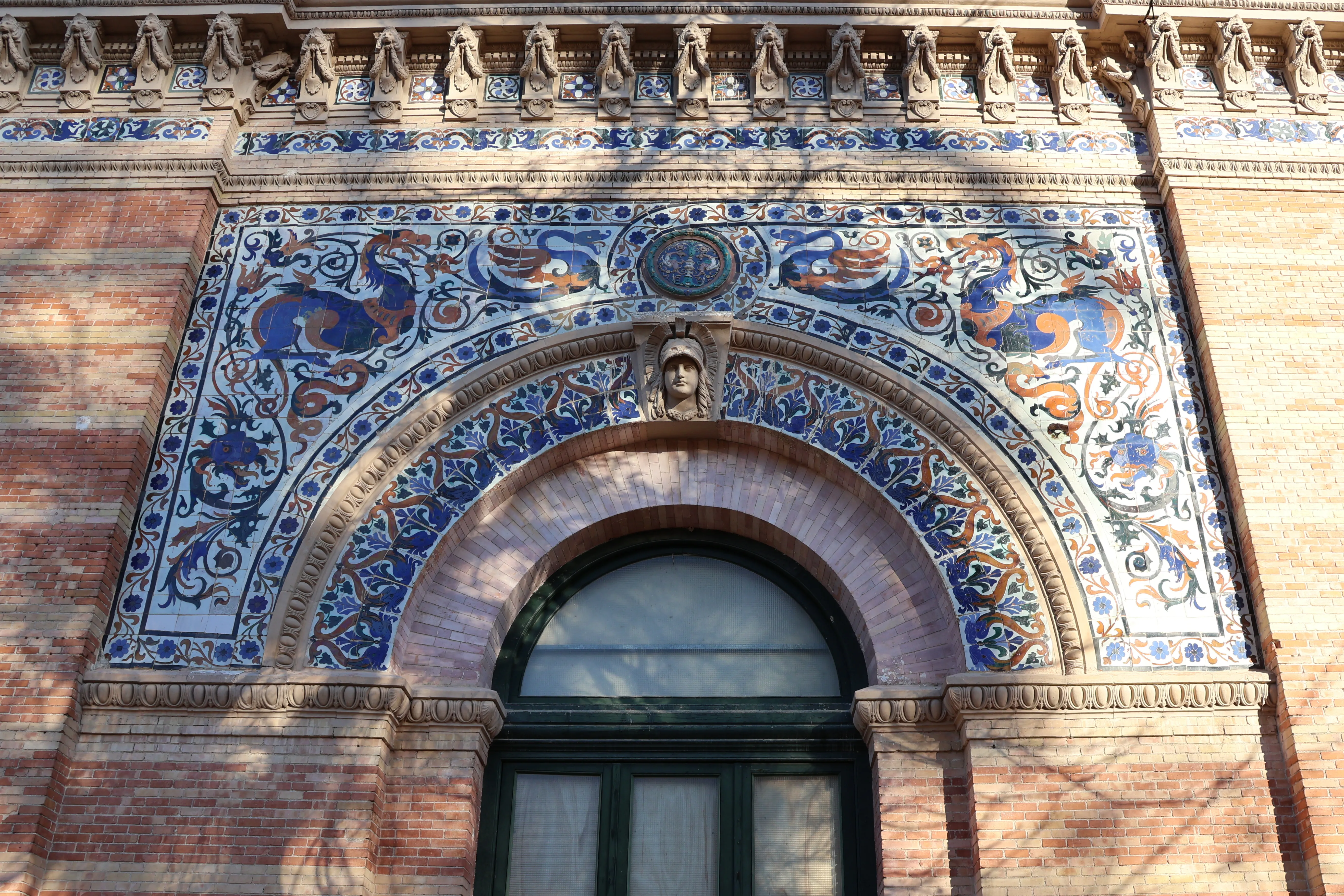 Azulejos ornamentales azules y naranjas sobre una ventana arqueada en un edificio de ladrillos