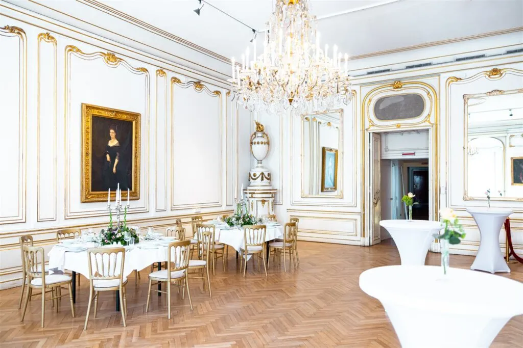 Barokke interieurkamer met witte muren, gouden versieringen, een kroonluchter en tafels gedekt voor een evenement