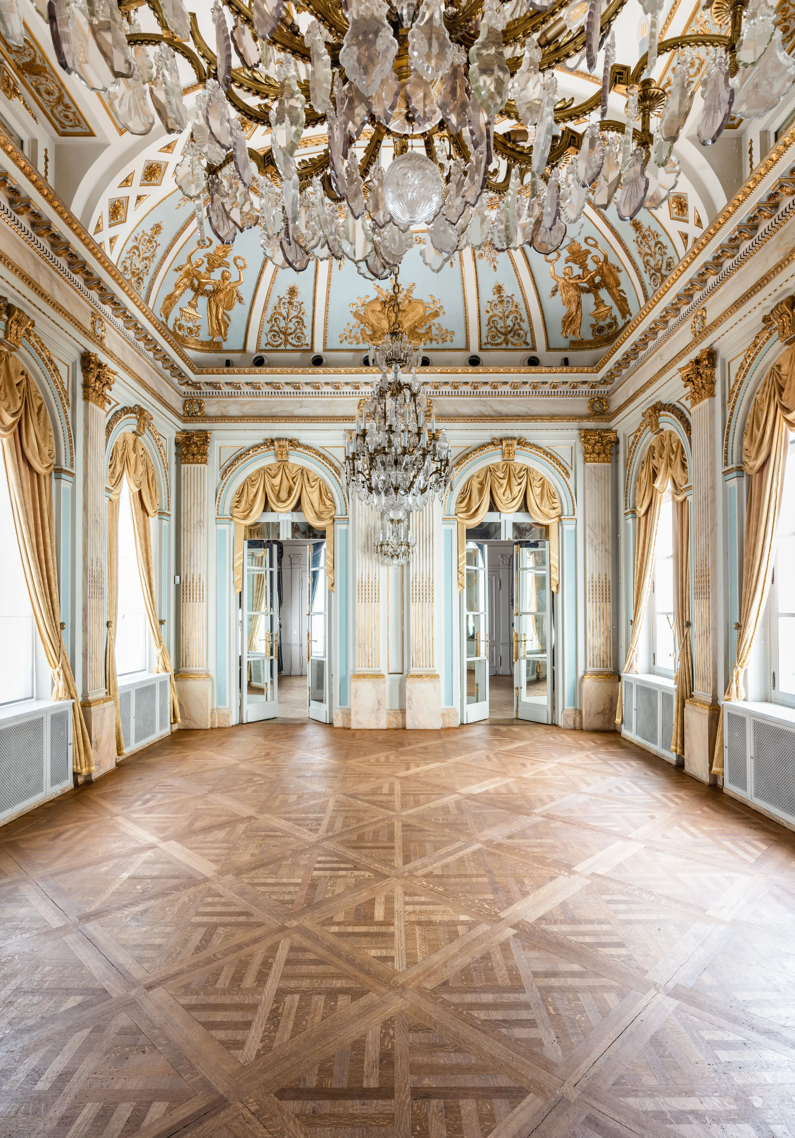 Gran salón de baile rococó con lámparas de araña de cristal, frescos dorados en el techo, puertas arqueadas con cortinas de oro y suelo de parqué.