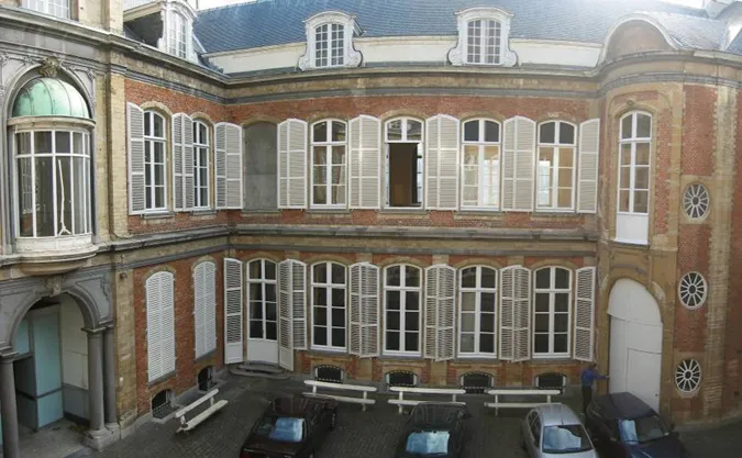 Vista aérea de la fachada del patio de ladrillo del Paleis op de Meir, con contraventanas blancas, ventanas arqueadas con una cúpula verde y coches aparcados debajo