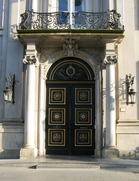 Puerta de entrada ornamentada en negro y oro del Paleis op de Meir con columnas blancas, detalles en piedra decorativos y balcón de hierro forjado encima