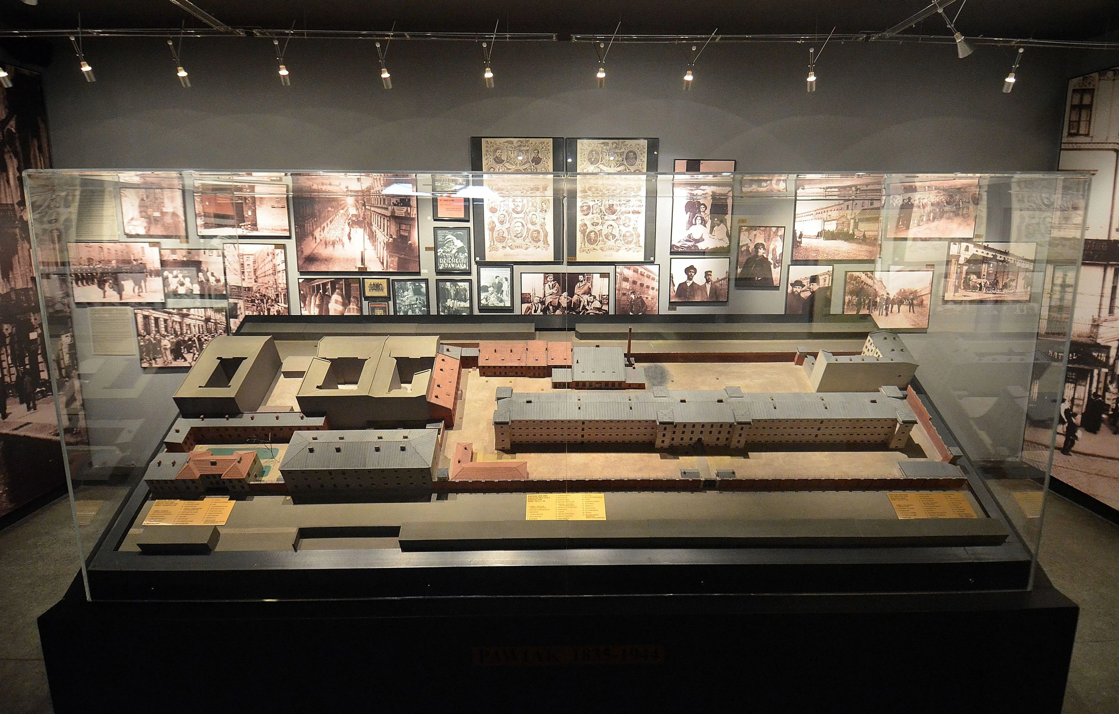 A scale model of Pawiak Prison inside a glass display case, surrounded by historical photographs on the wall