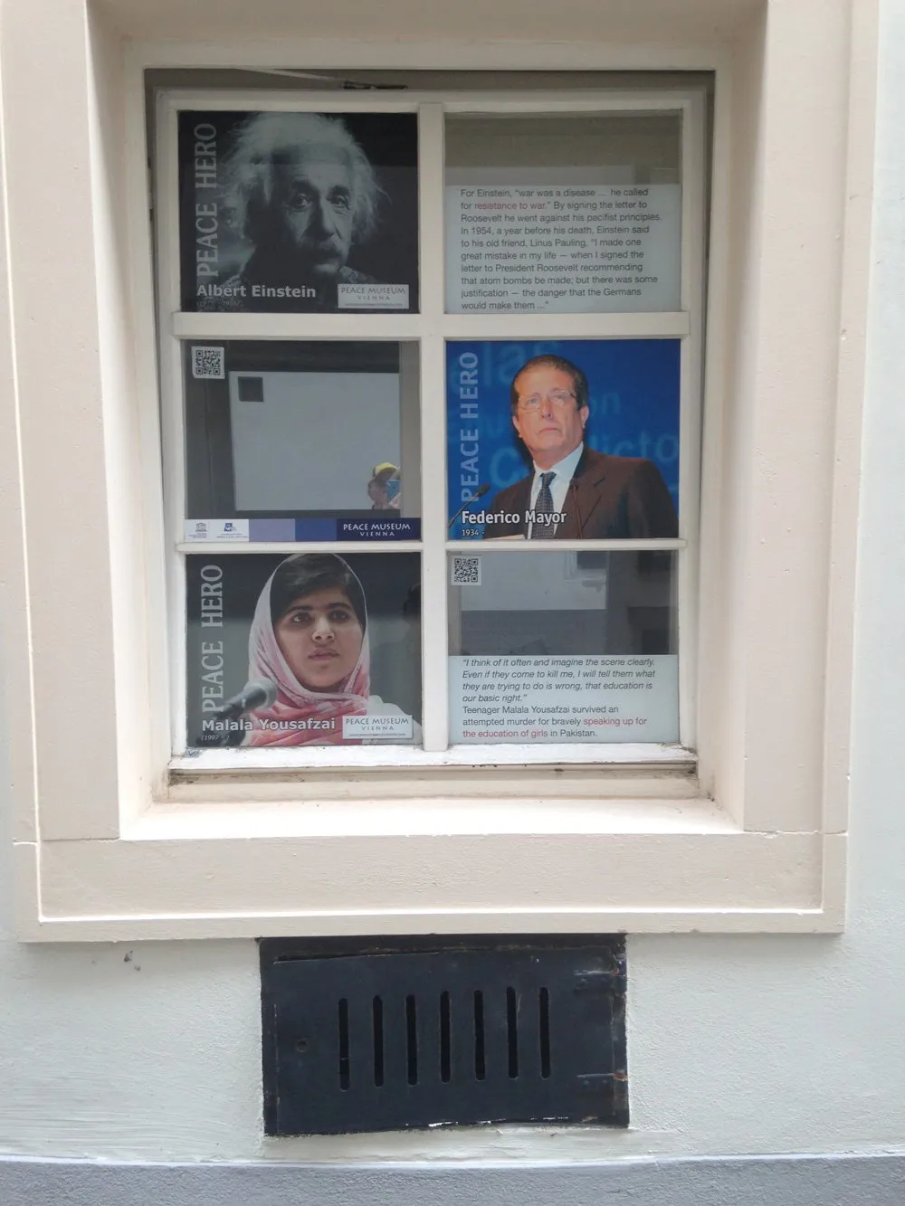 Vitrine met portretten van Albert Einstein, Federico Mayor en Malala Yousafzai, gelabeld als Vredeshelden, aan de buitenkant van een gebouw.