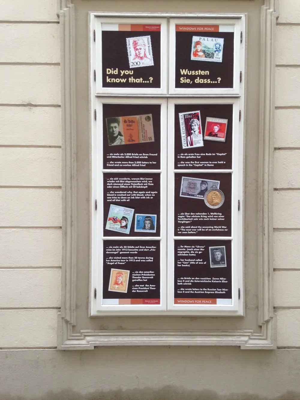 Zewnętrzne okno wystawowe Muzeum Pokoju w Wiedniu z panelami informacyjnymi i historycznymi zdjęciami na fasadzie budynku