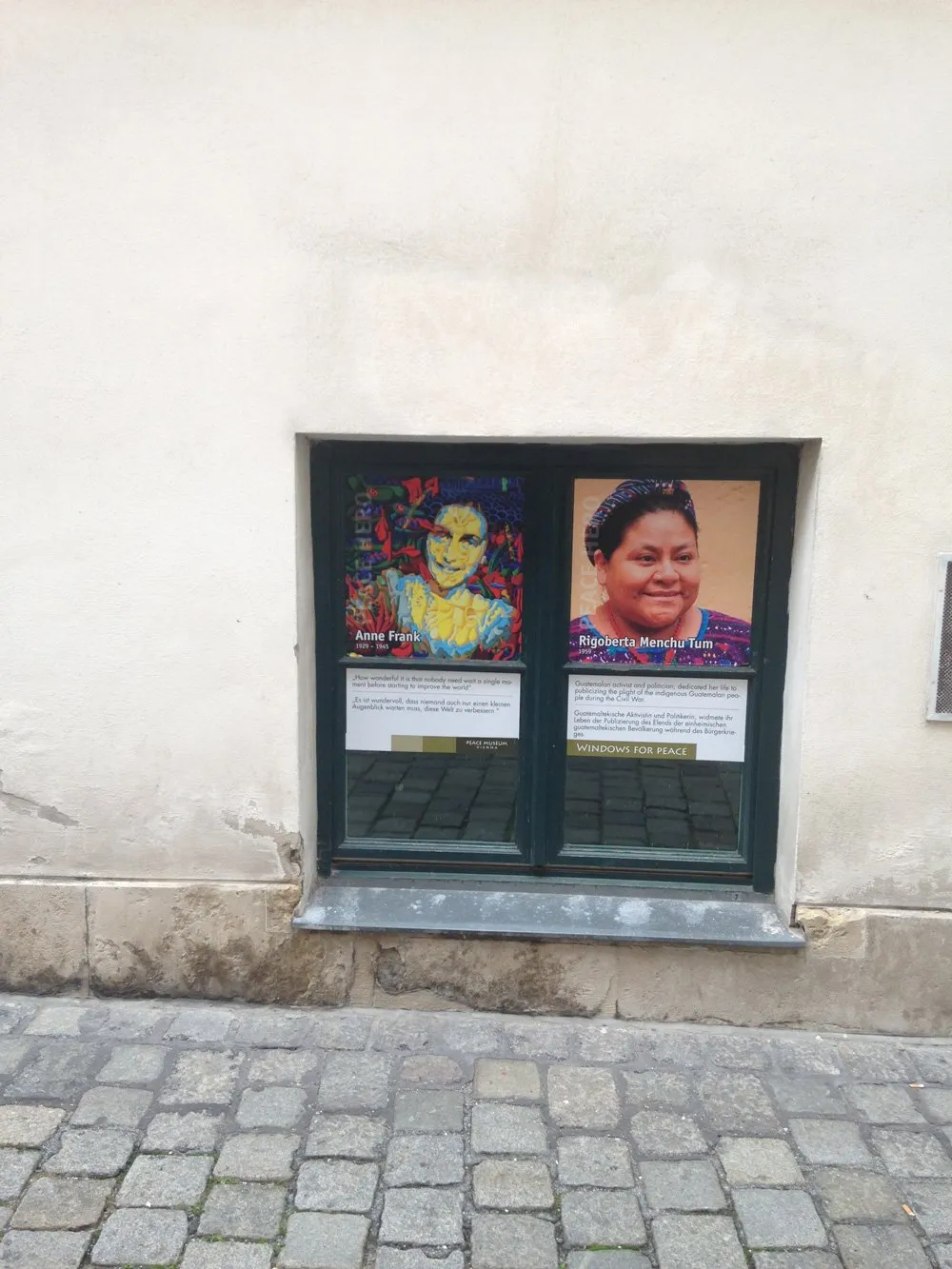 Vitrine met portretten van Anne Frank en Rigoberta Menchú op een gebouwgevel