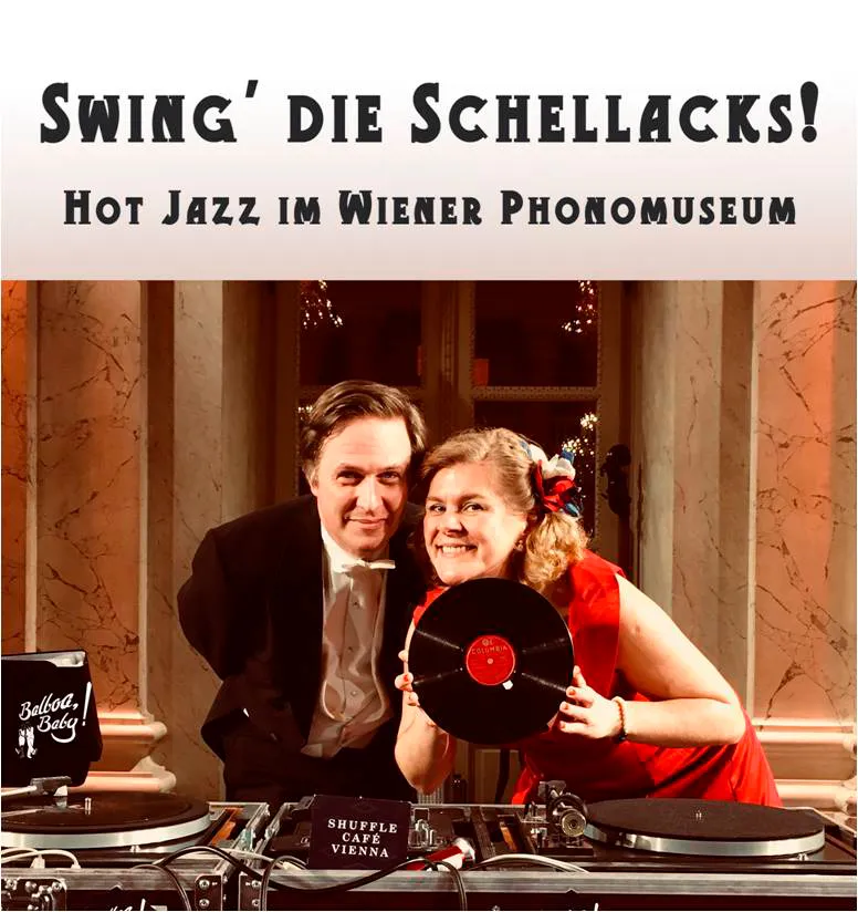 Two people posing with a vinyl record and turntables in front of a marble wall with text 'SWING' DIE SCHELLACKS! HOT JAZZ IM WIENER PHONOMUSEUM'