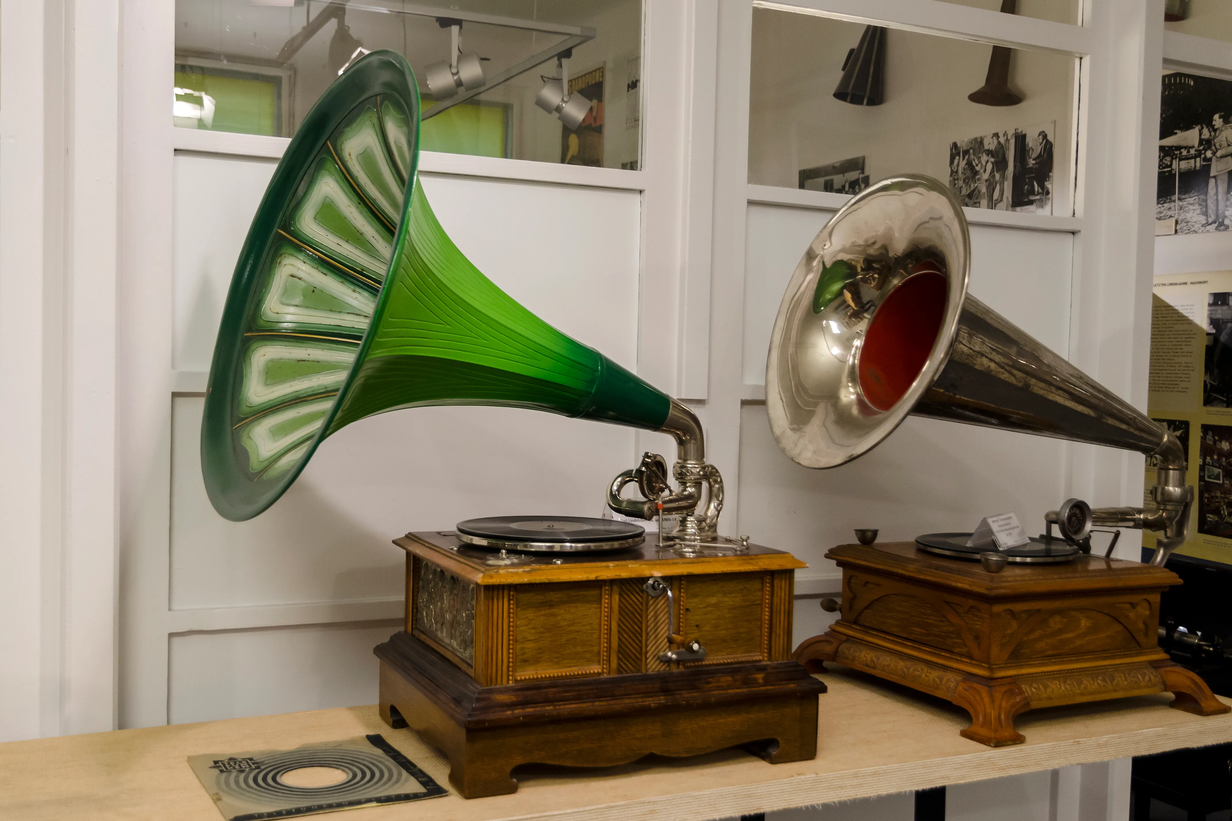 Twee vintage grammofoons met een groene en een zilveren hoorn op houten standaards