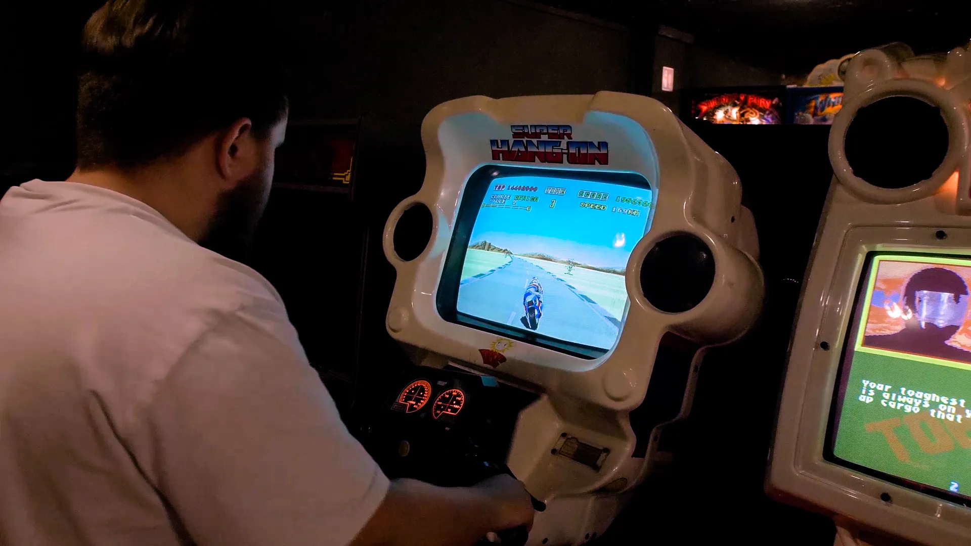 Persona jugando a un juego de arcade retro en una cabina blanca con una pantalla que muestra un juego de carreras de motos