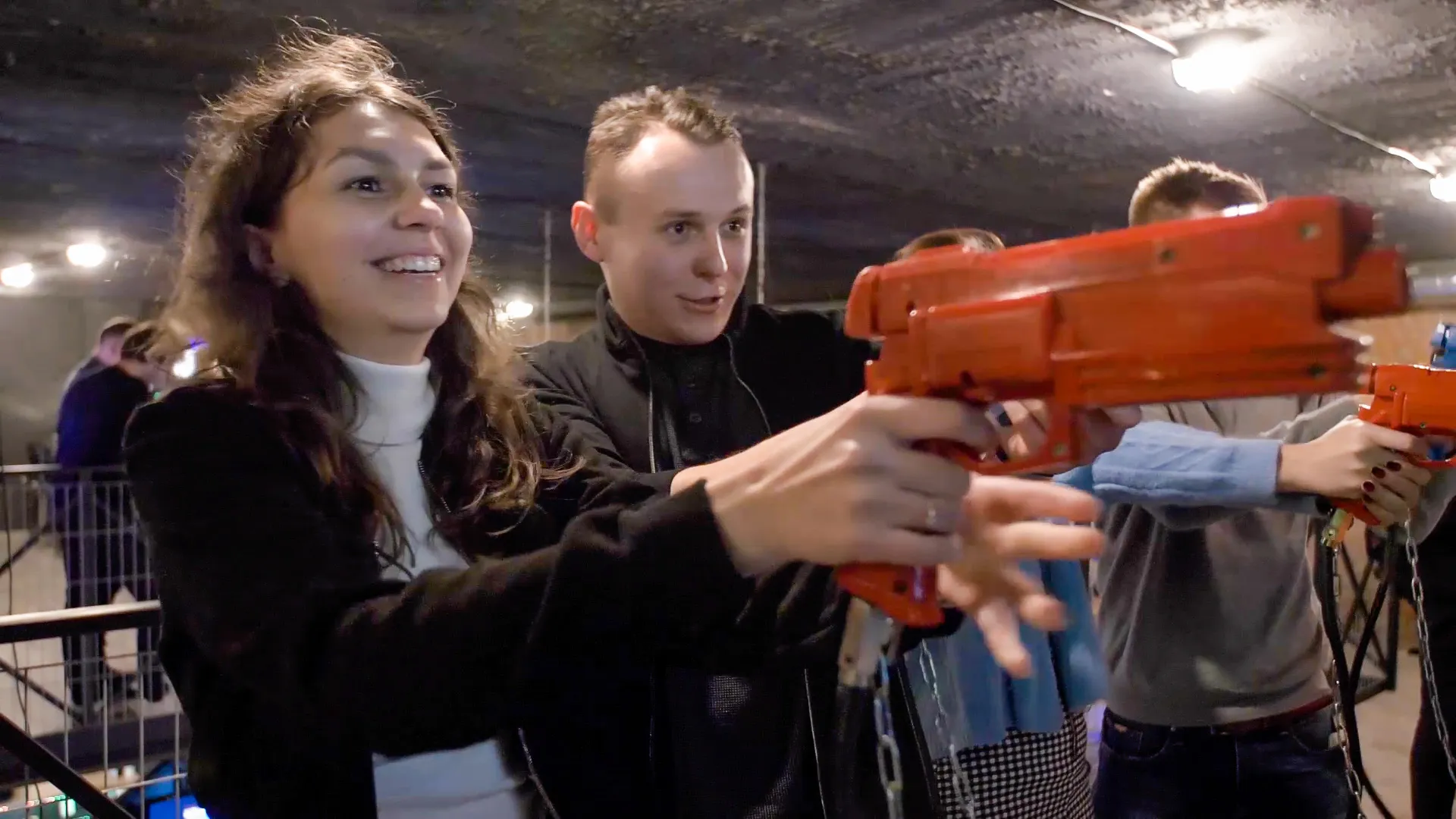 Dos personas jugando a un juego de disparos arcade rojo en una sala de juegos cubierta.