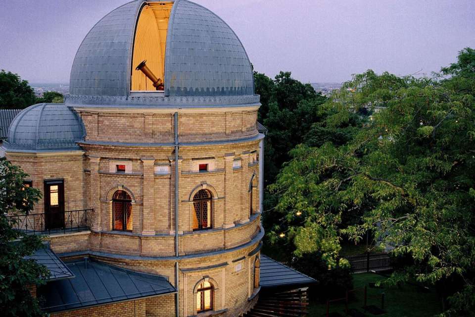 Budynek Planetarium Wien z dużą kopułą i łukowatymi oknami, otoczony drzewami pod niebem o zmierzchu