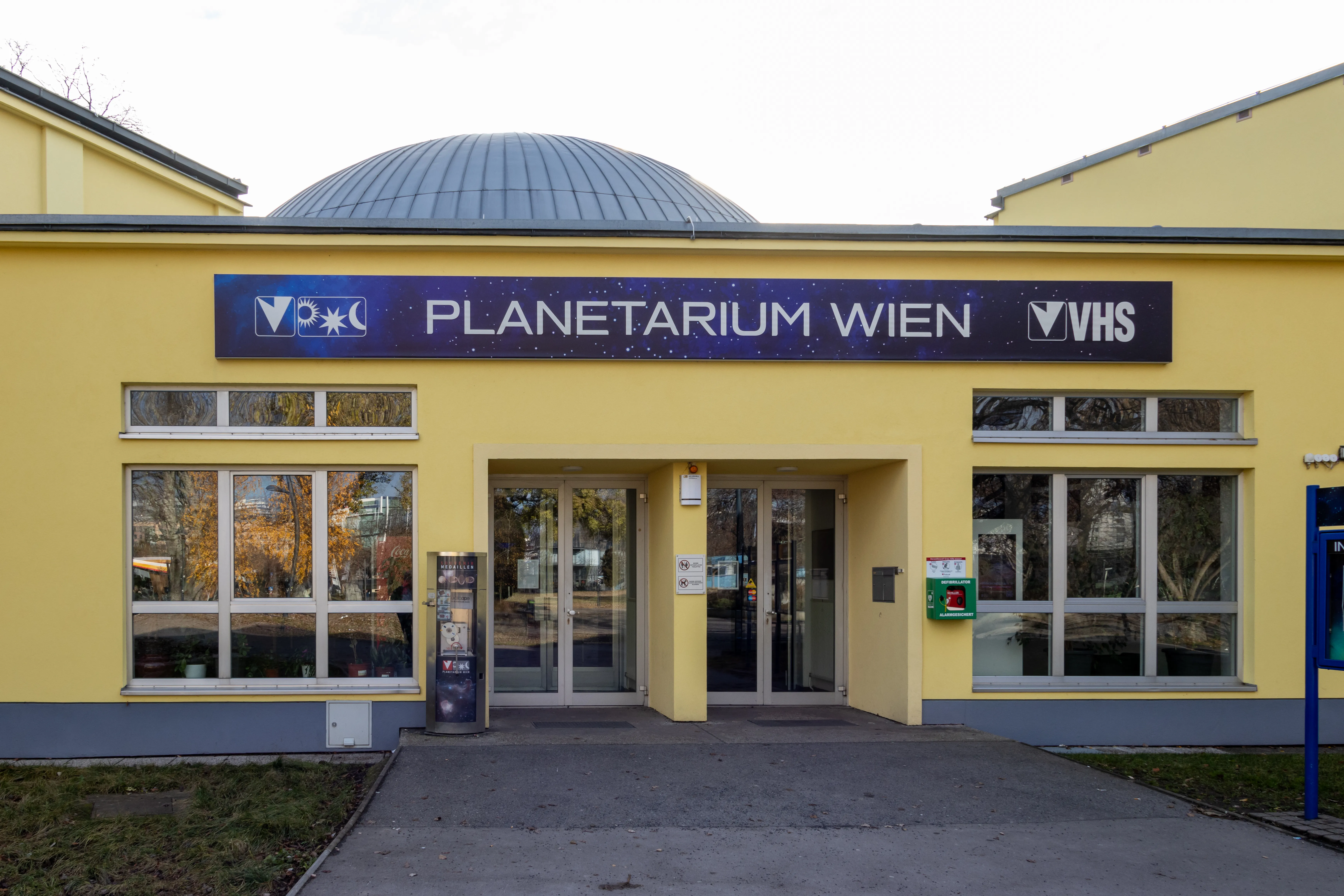 Geel gebouw met een koepel en een bord met de tekst 'Planetarium Wien' en 'VHS'
