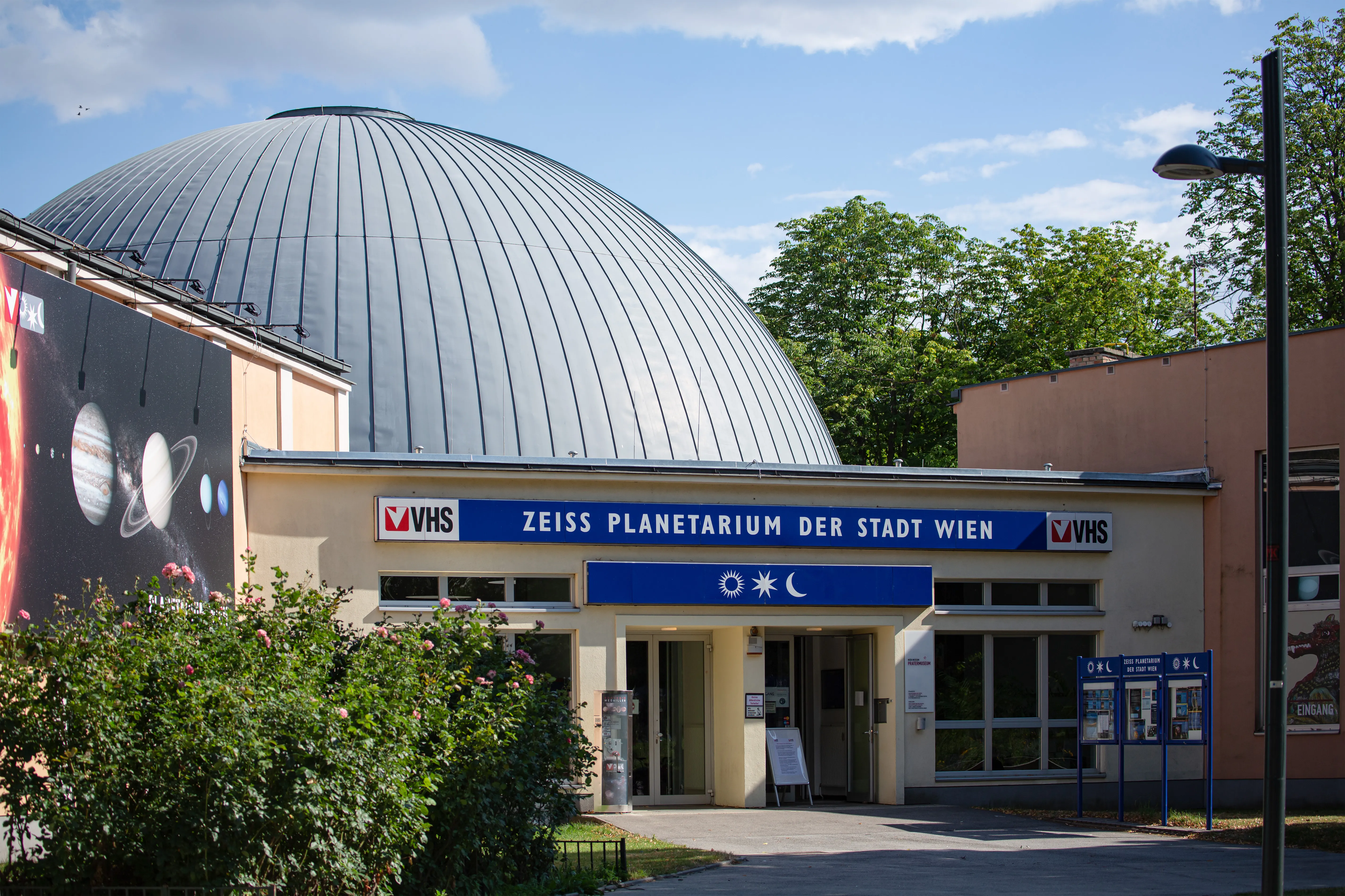 Het Planetarium Wien met zijn grote zilveren koepel en ingangsnaambord met de tekst 'ZEISS PLANETARIUM DER STADT WIEN' onder een blauwe hemel.