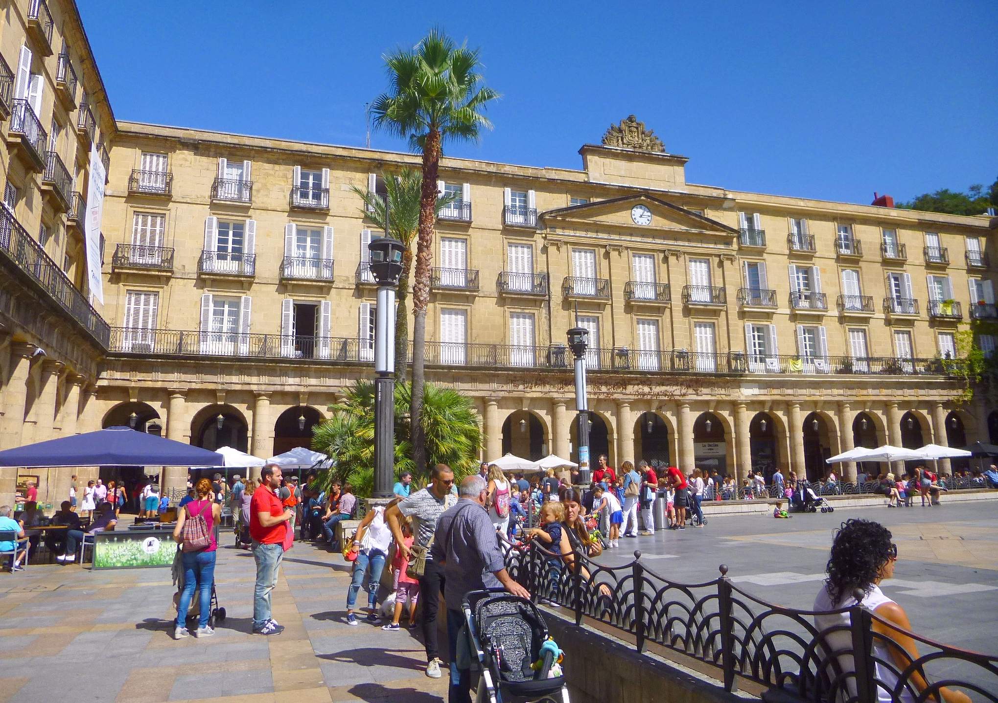 Neoklasycystyczna arkadowa fasada Plaza Nueva w Bilbao z ludźmi zgromadzonymi na placu pod bezchmurnym niebem